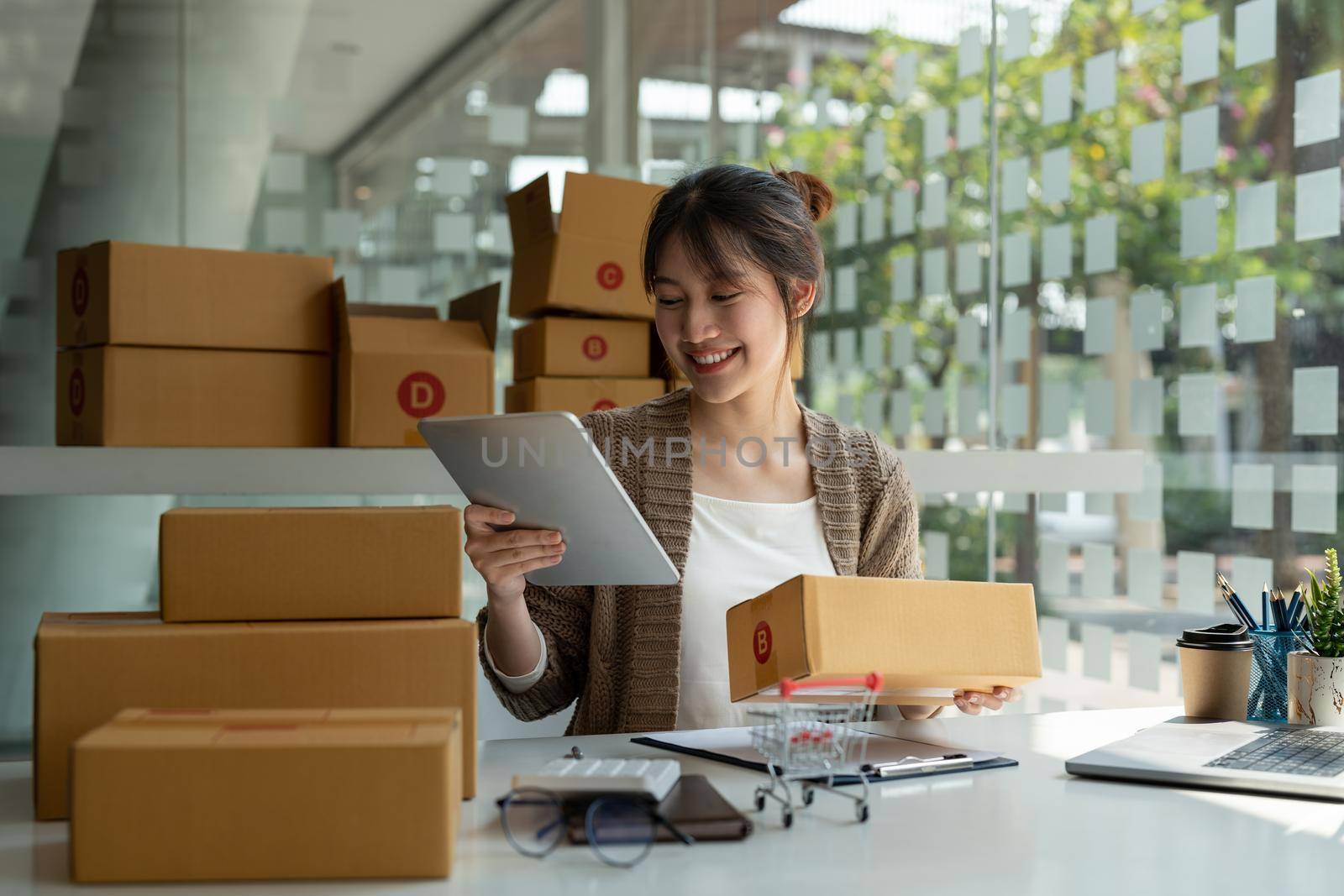 Sell online, Young asian woman checking order and customer's details and addresses on laptop or box in order to prepare for shipping according to the information, Online shopping SME entrepreneur.