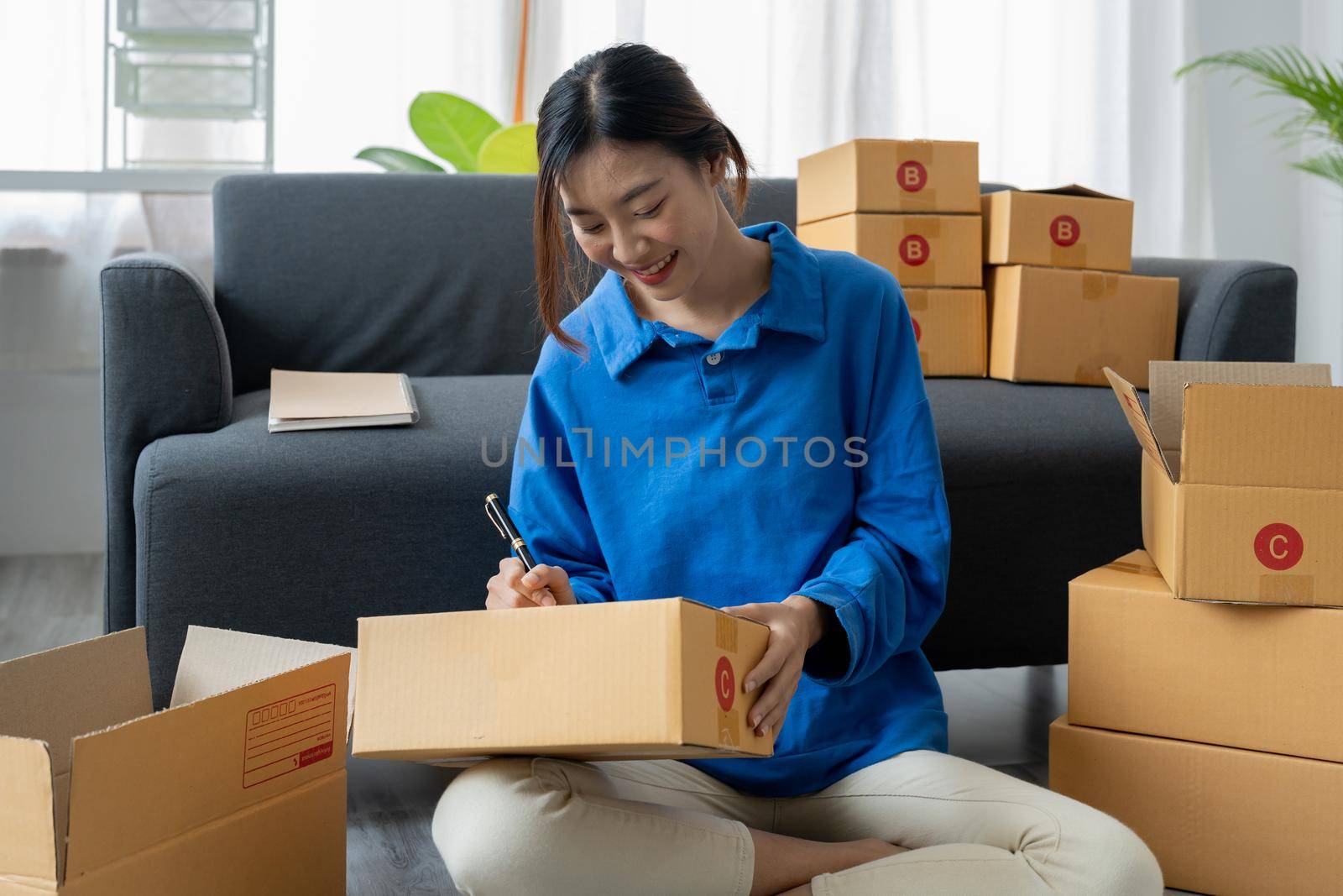 Shipping shopping online, startup small business owner writing address on cardboard box at workplace. Freelance Asian woman small business entrepreneur SME working with box at home.