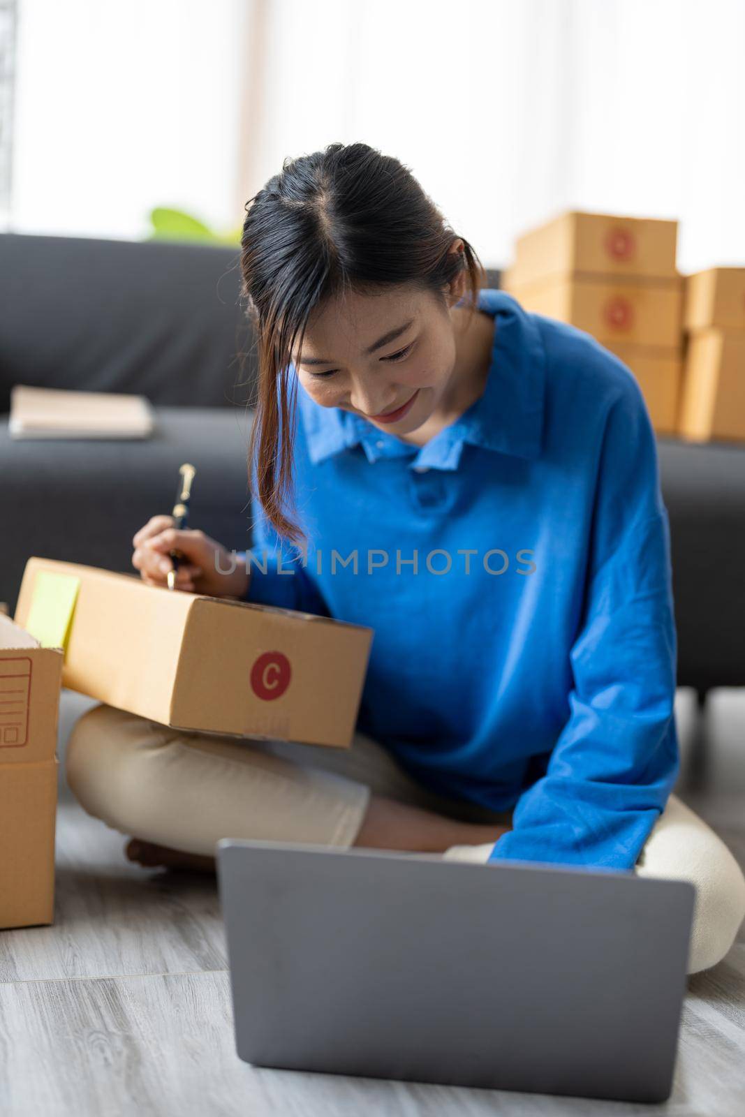 Shipping shopping online, startup small business owner writing address on cardboard box at workplace. Freelance Asian woman small business entrepreneur SME working with box at home by nateemee