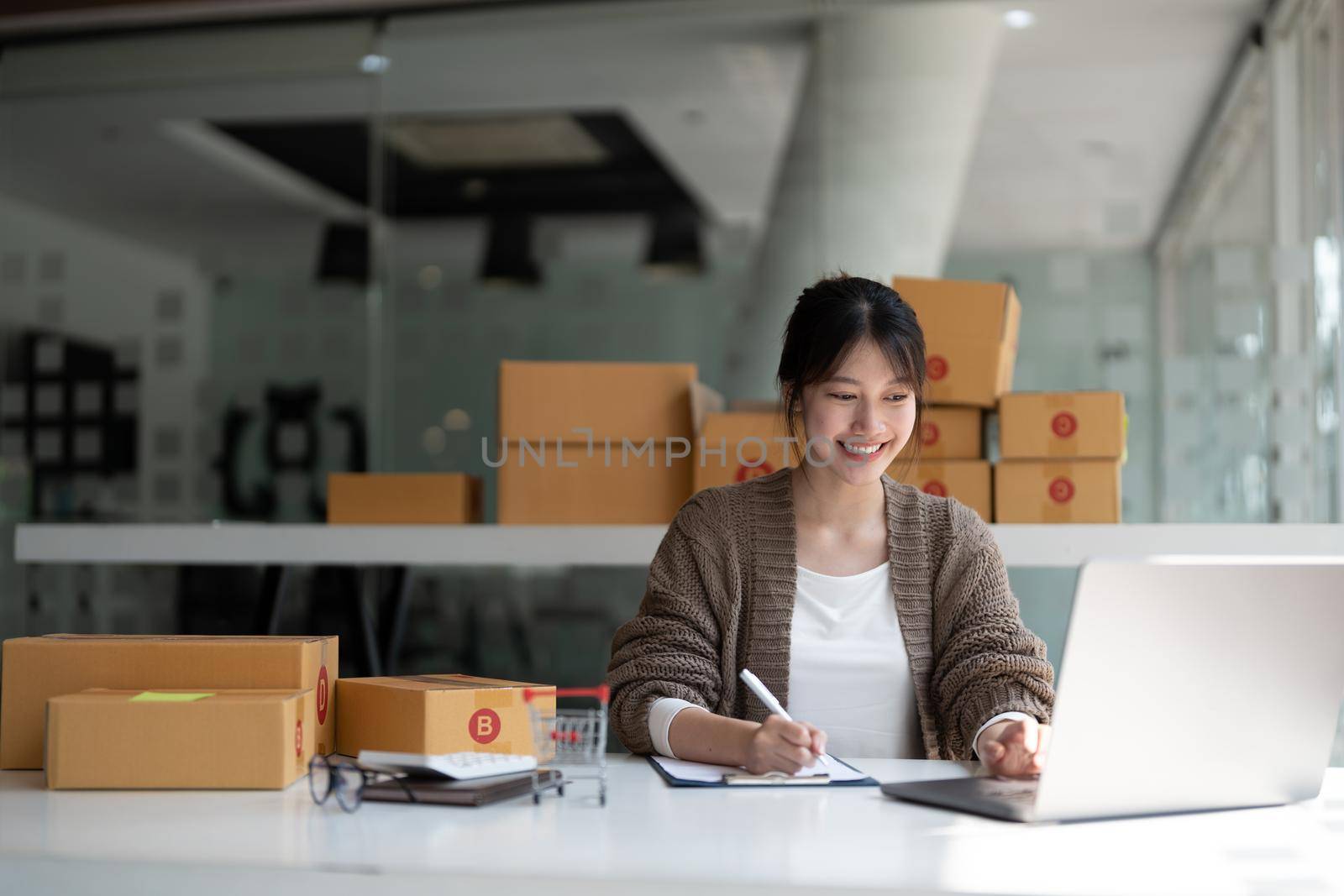 Sell online, Young asian woman checking order and customer's details and addresses on laptop or box in order to prepare for shipping according to the information, Online shopping SME entrepreneur.