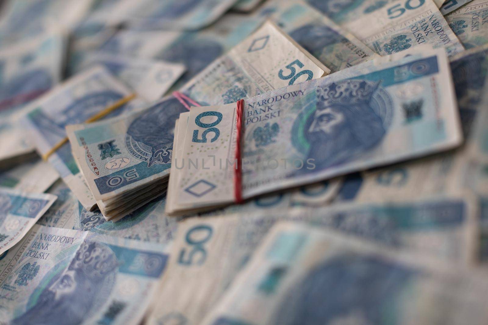 A file of cash bound with a rubber band lies on top of loosely and randomly distributed fifty dollar paper bills.