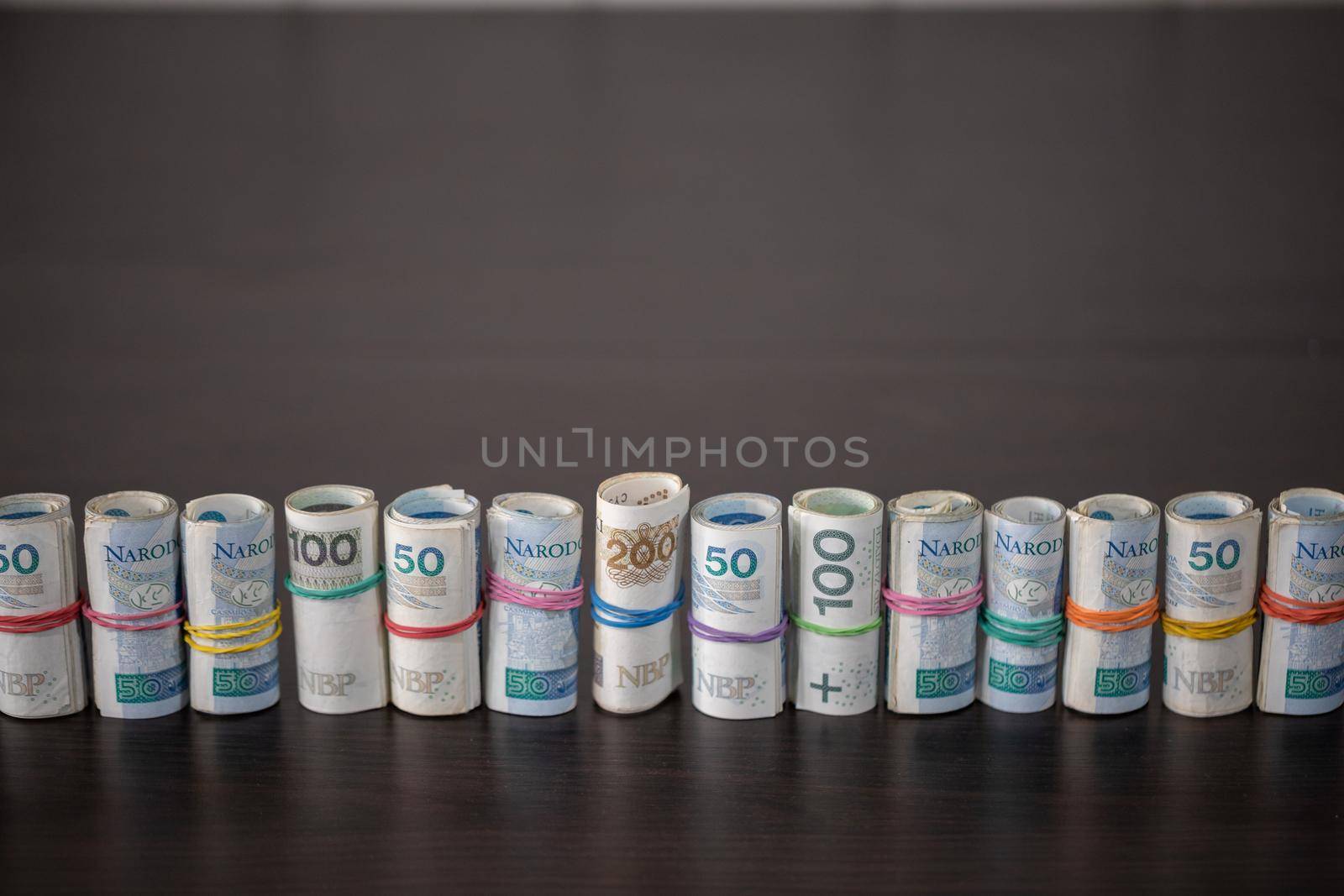 A collection of multiple denominations of Polish national currency rolled up and compressed with a rubber band.