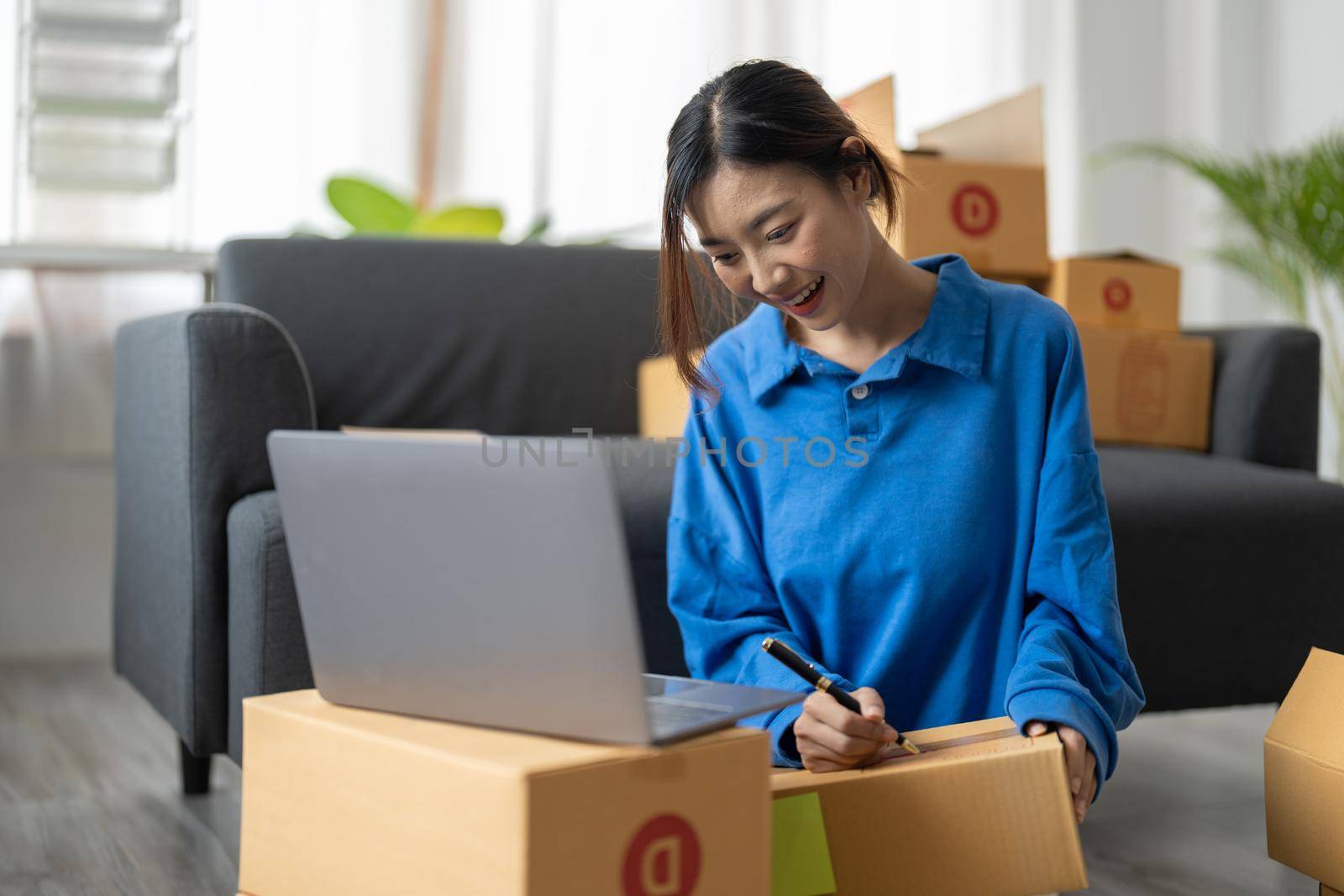 Shipping shopping online, startup small business owner writing address on cardboard box at workplace. Freelance Asian woman small business entrepreneur SME working with box at home.