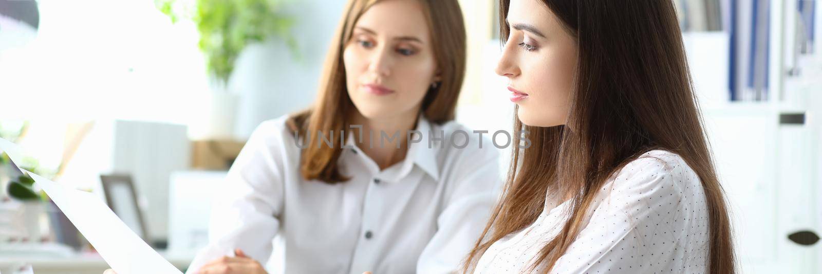 Portrait of joyful businesswoman sitting indoors with friendly colleague and looking at important project in paper folder with charts and graphs. Accounting office concept
