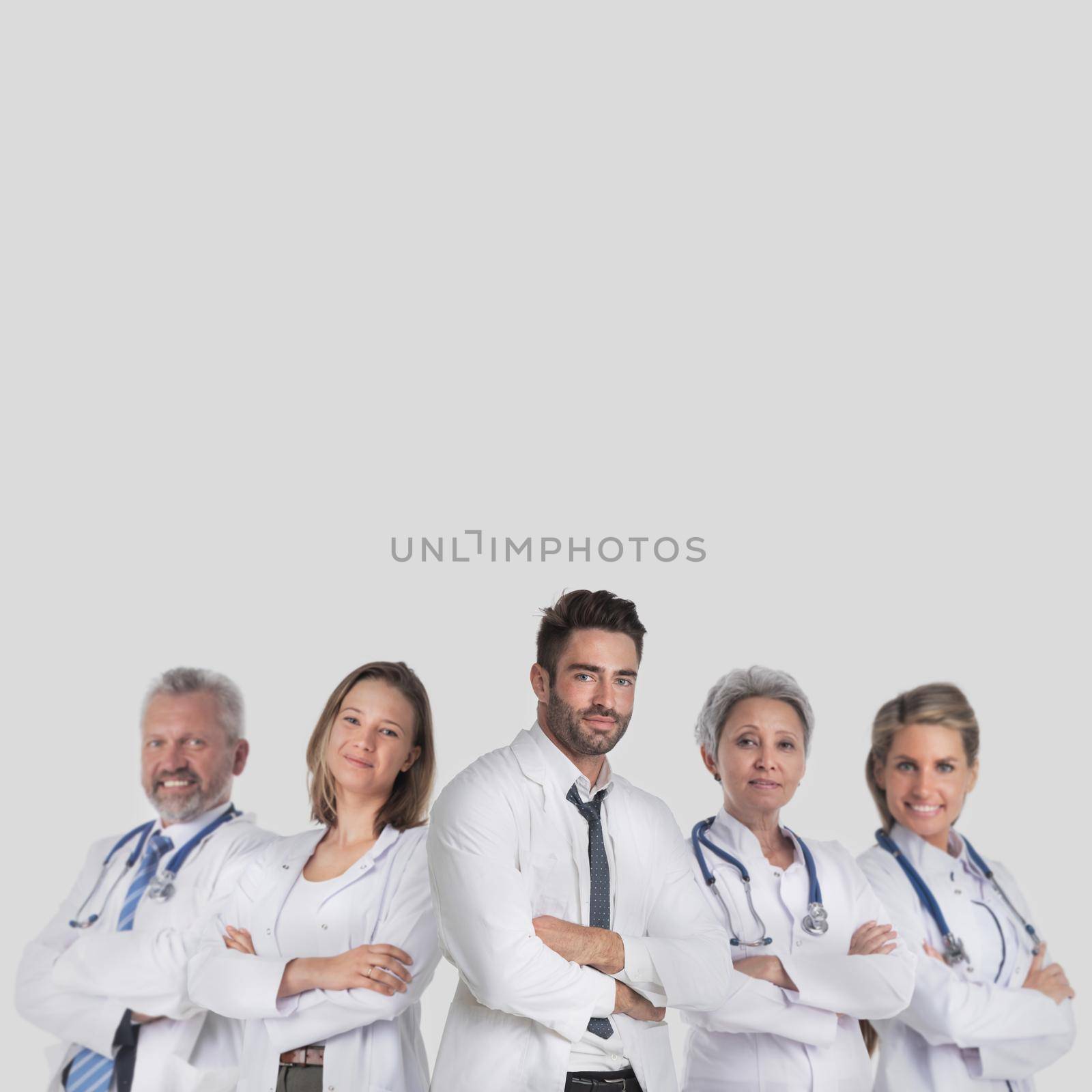 Group of successful medical doctors in labcoat uniform standing together with arms folded isolated on gray background with copy space for text