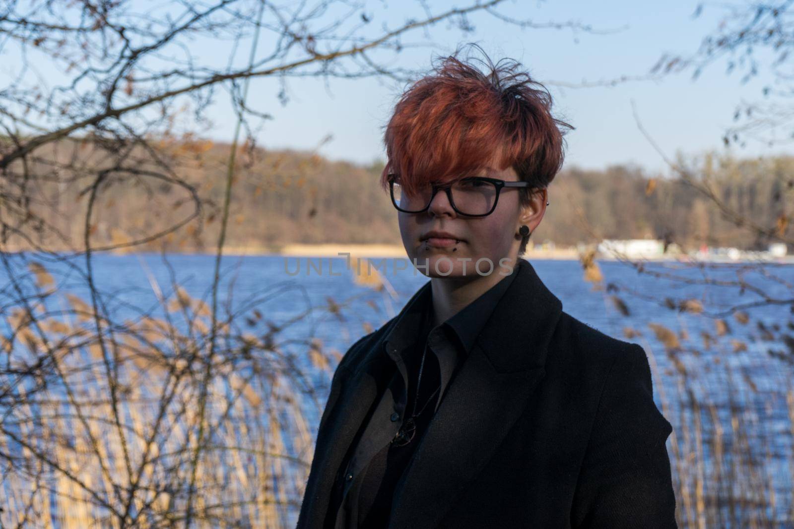 young girl with glasses with short haircut and piercing on her face against the background of nature.