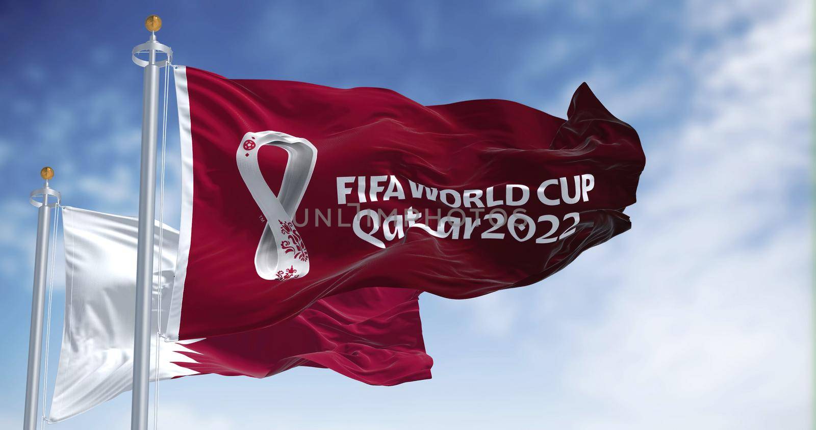 Doha, Qatar, January 2022: Flags Qatar 2022 World Cup logo waving among Qatar national flag in the wind. The event is scheduled in Qatar from 21 November to 18 December 2022