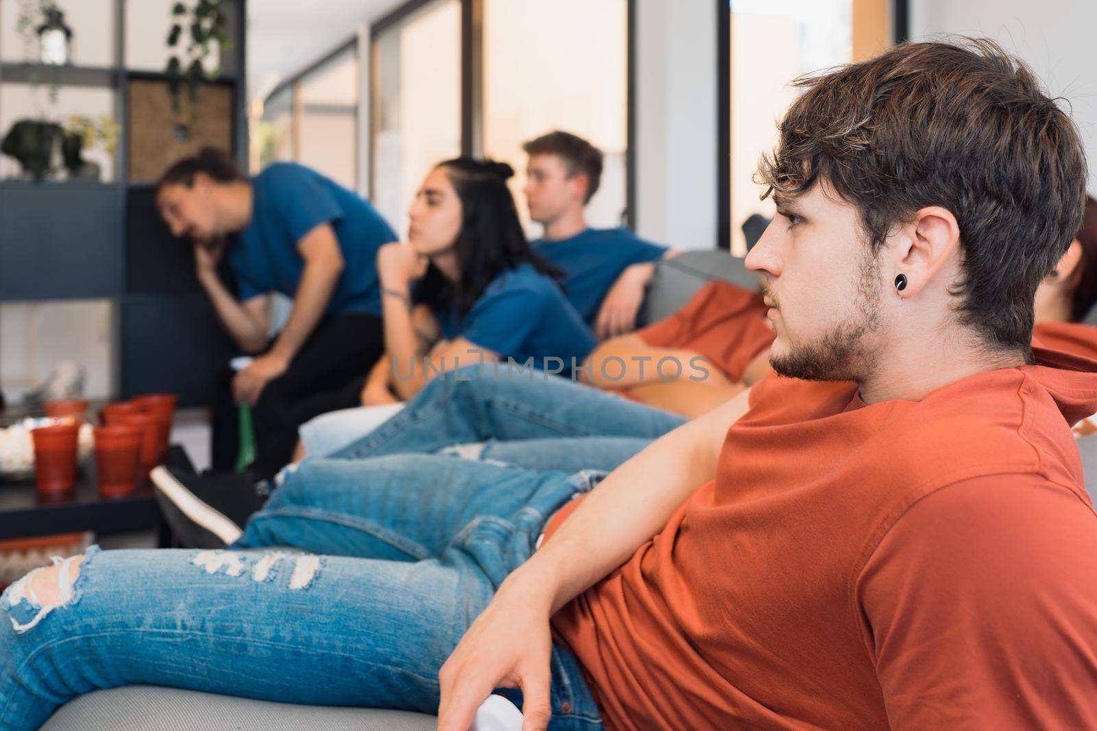 group of young people, bored, watching a football match on tv. tired youngster friends, at a house party. leisure by CatPhotography