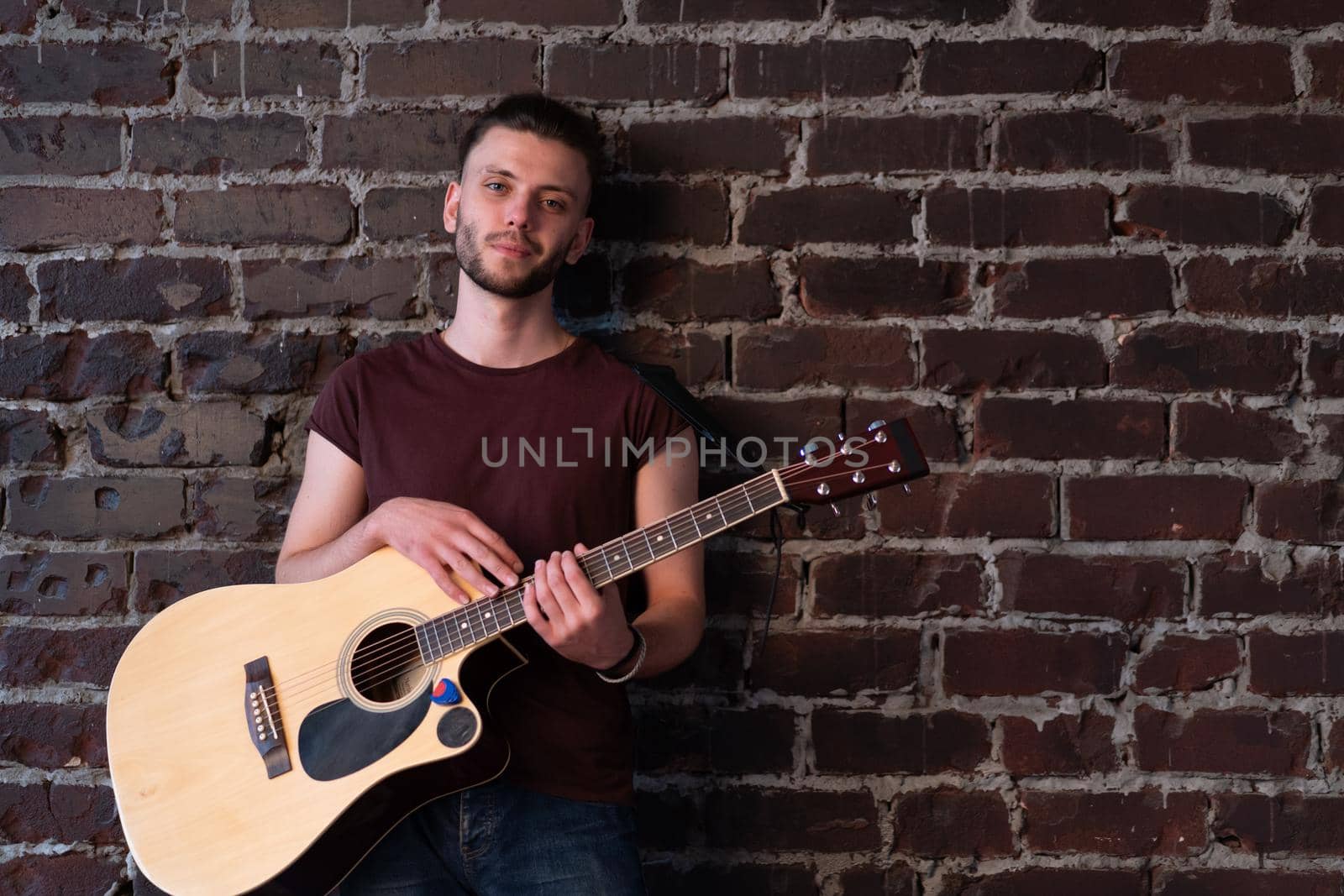 Man with acoustic guitar against brick wall playing music singing songs enjoy life Handsome caucasian male guitar player practice play musical instrument home loft interior Creative lifestyle hobby