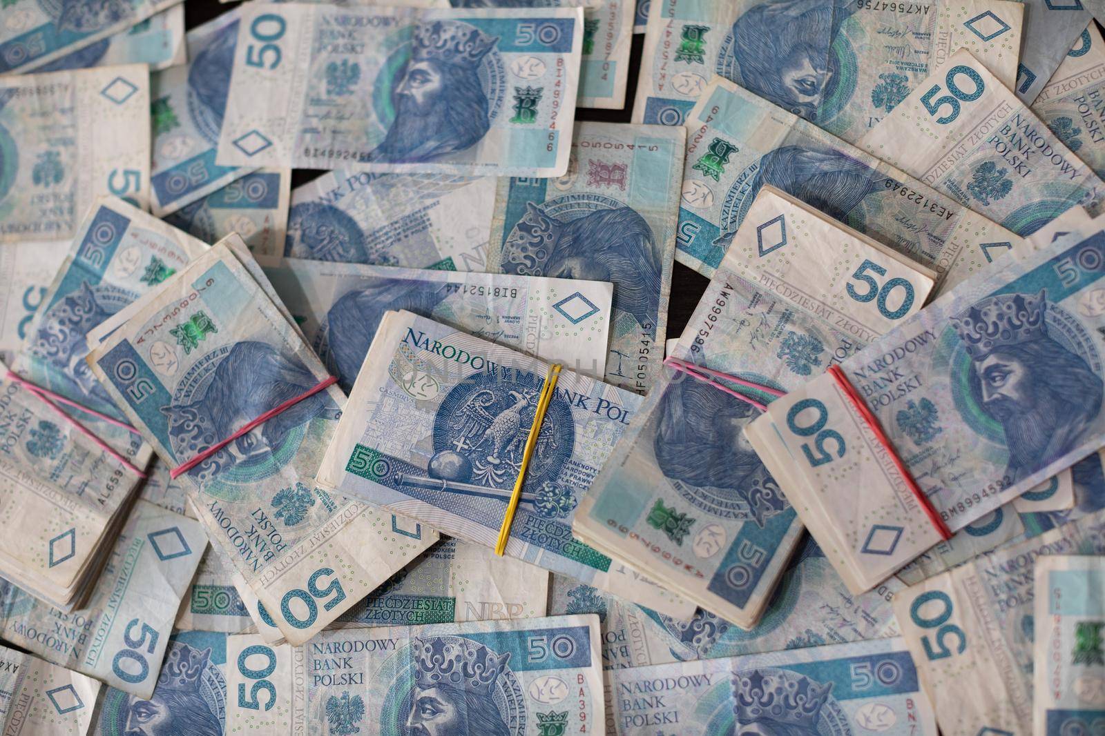 A file of cash bound with a rubber band lies on top of loosely and randomly distributed fifty dollar paper bills.