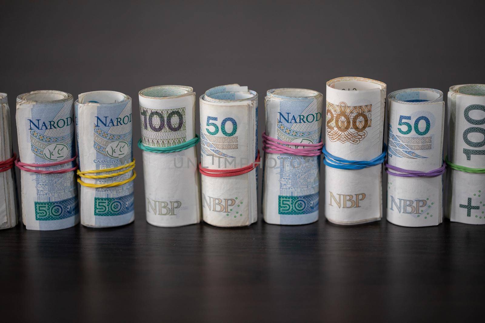 A collection of multiple denominations of Polish national currency rolled up and compressed with a rubber band.