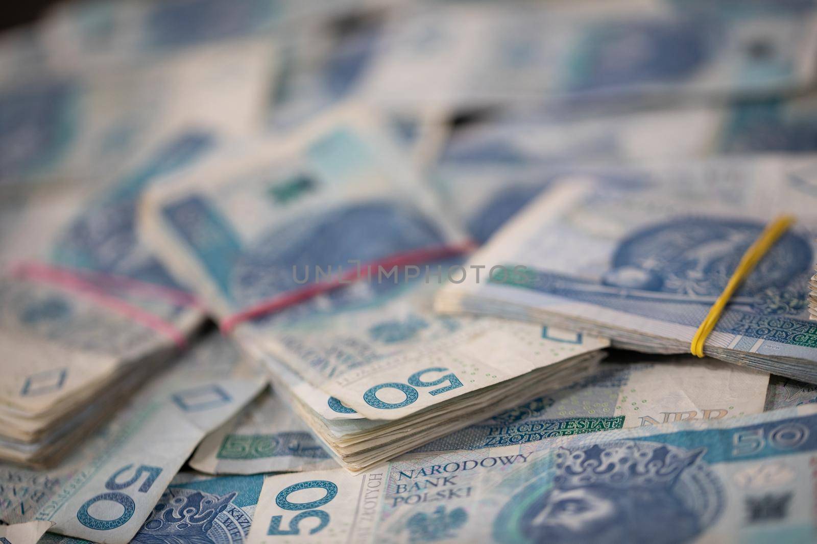A file of cash bound with a rubber band lies on top of loosely and randomly distributed fifty dollar paper bills.