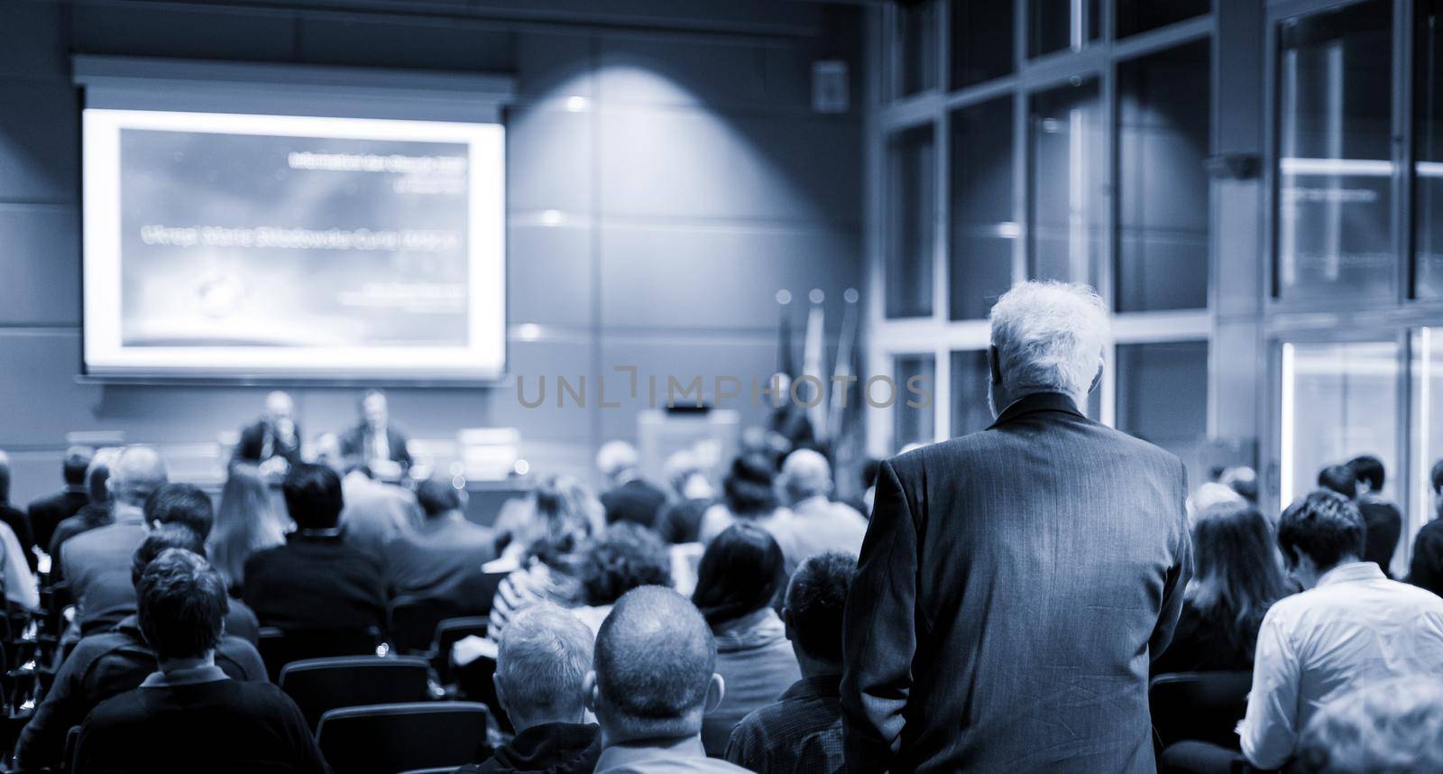 I have a question. Group of business people sitting at the chairs in conference hall. Businessman raising his arm. Conference and Presentation. Business and Entrepreneurship.