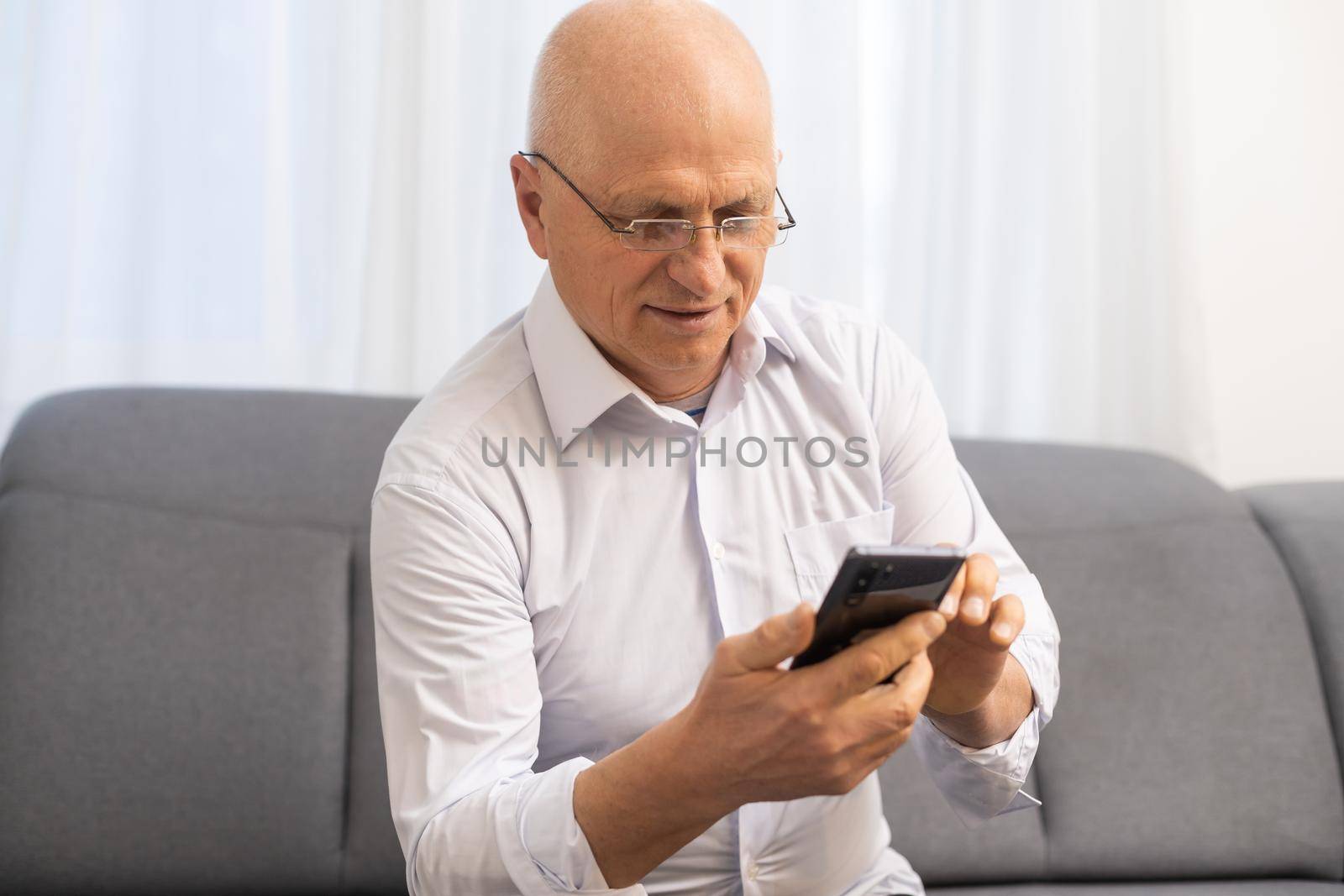 Closeup portrait headshot elderly man with glasses having seeing cell phone has vision problems. by Andelov13