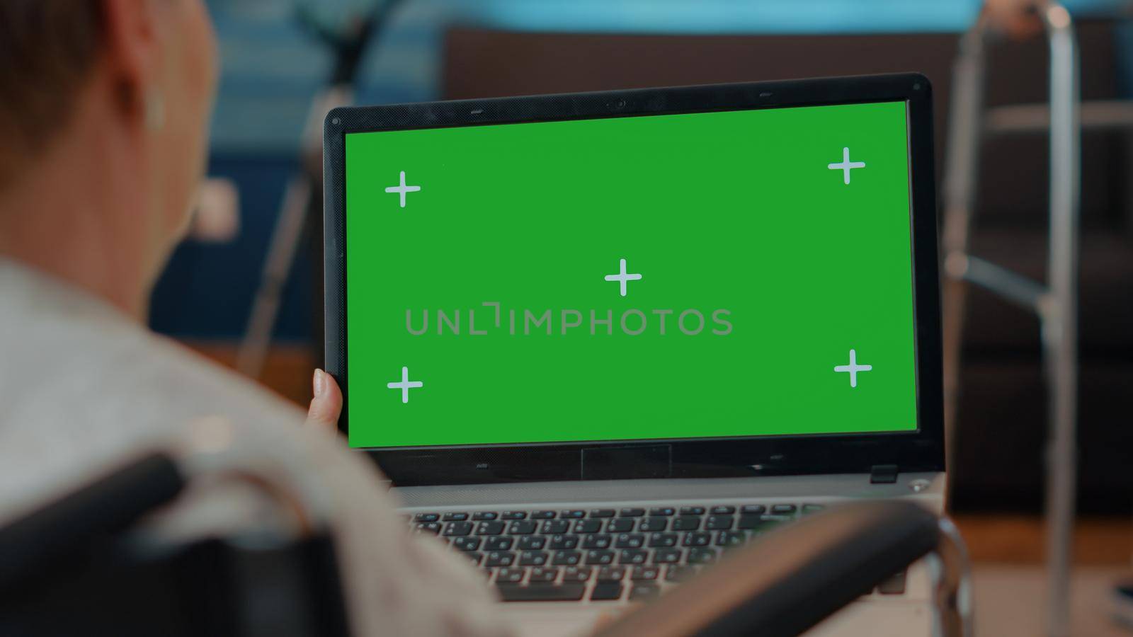 Elder person with disability using green screen on laptop, looking at isolated mock up template and blank copy space. Woman sitting in wheelchair with chroma key background on computer.