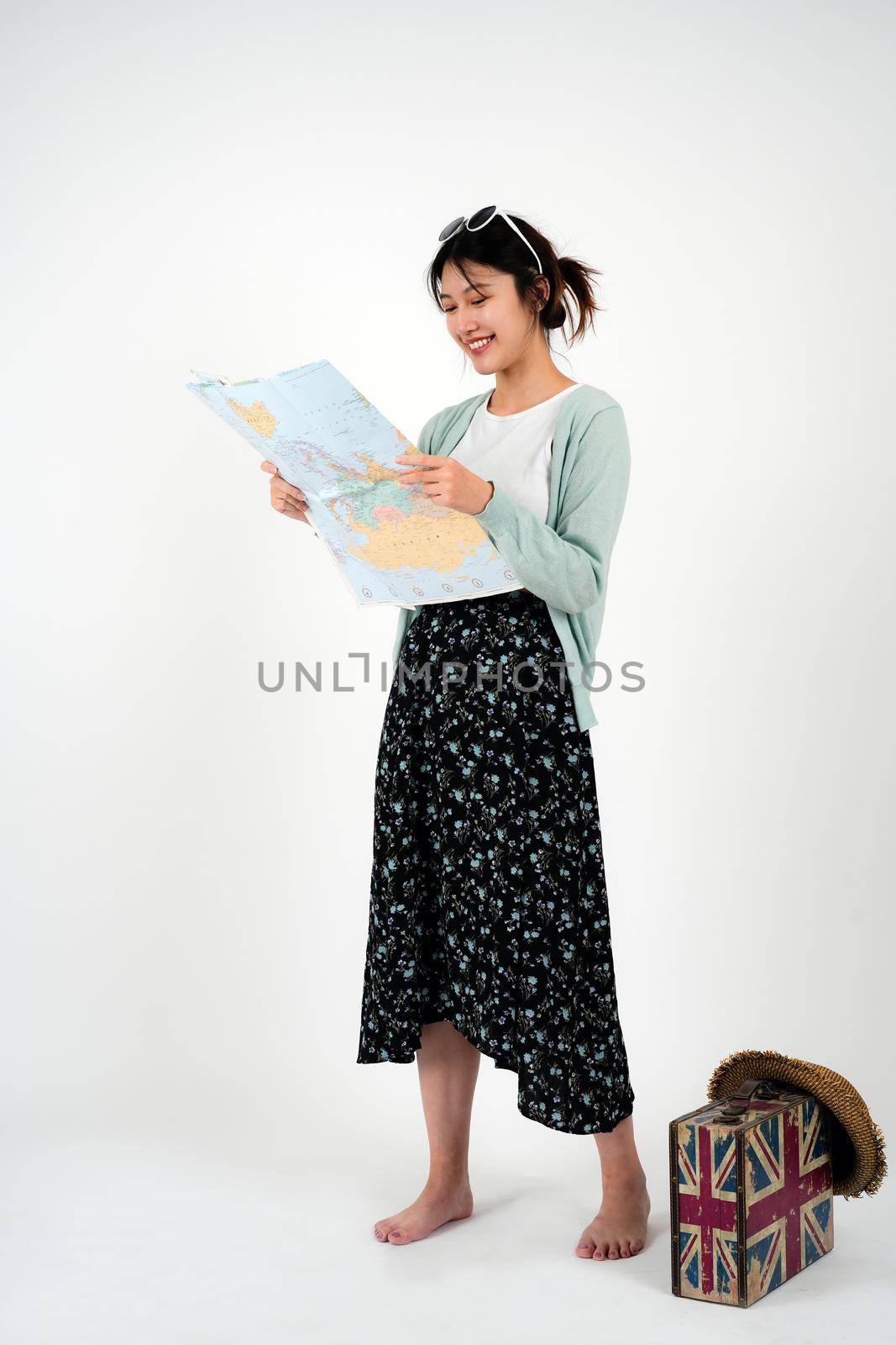 Positive smiling young asian female tourist searches for inspiring places, holds paper map, finds new sightseeing for discovering, wears round spectacles, isolated on white studio wall.