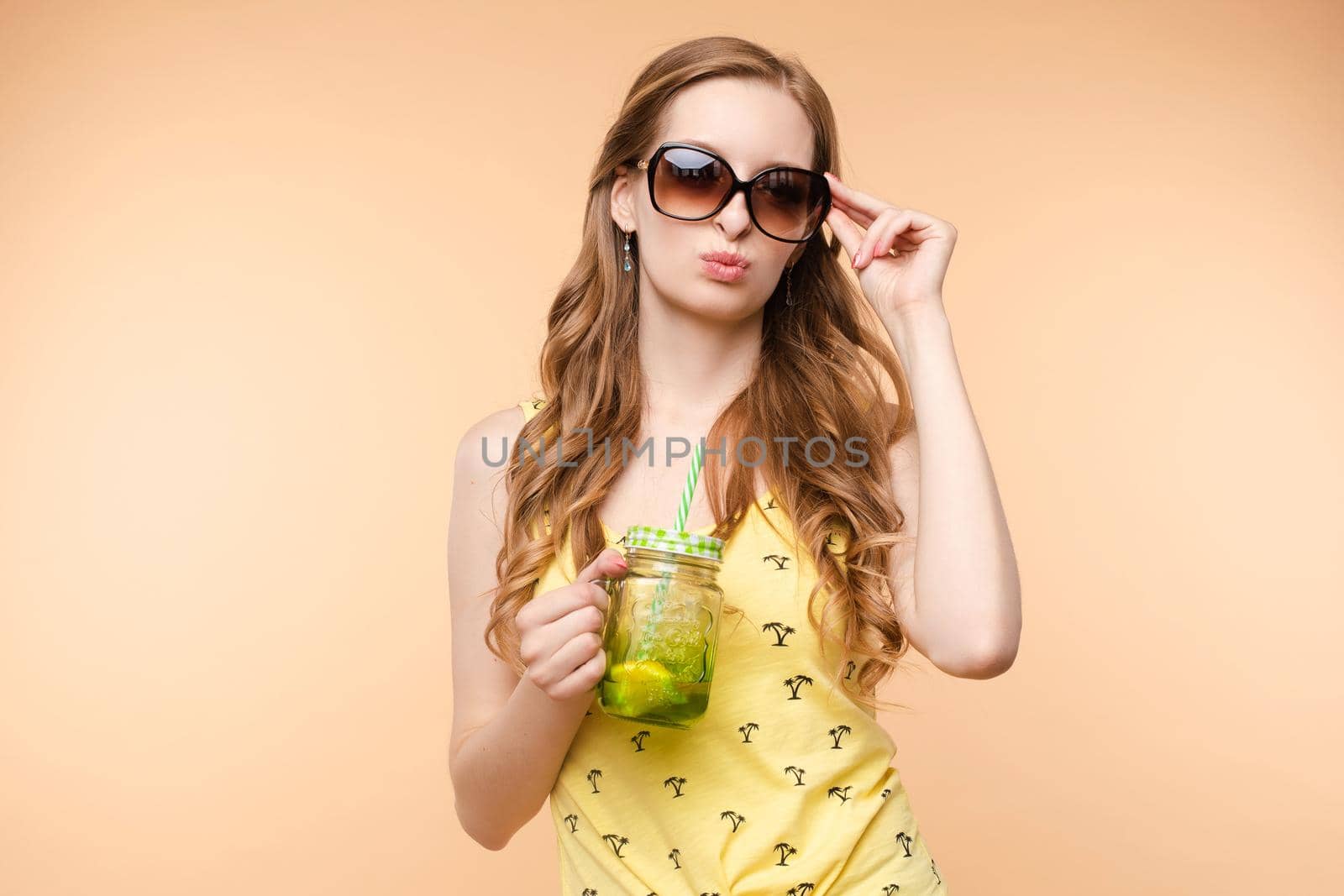 A beautiful woman with a glass of chilled drink in bright clothes on a bright isolated background in the studio..