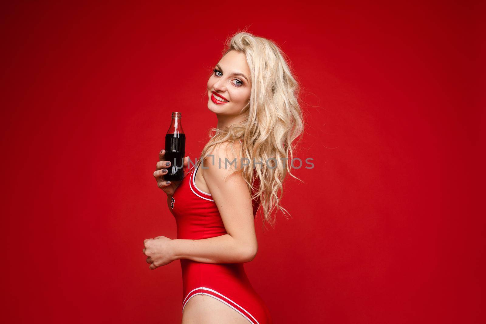 Portrait of young smiling blond model in summer swimwear red bathing suit. Sexy carefree woman having fun and going crazy. Female posing near wall in studio. Cheerful and happy.