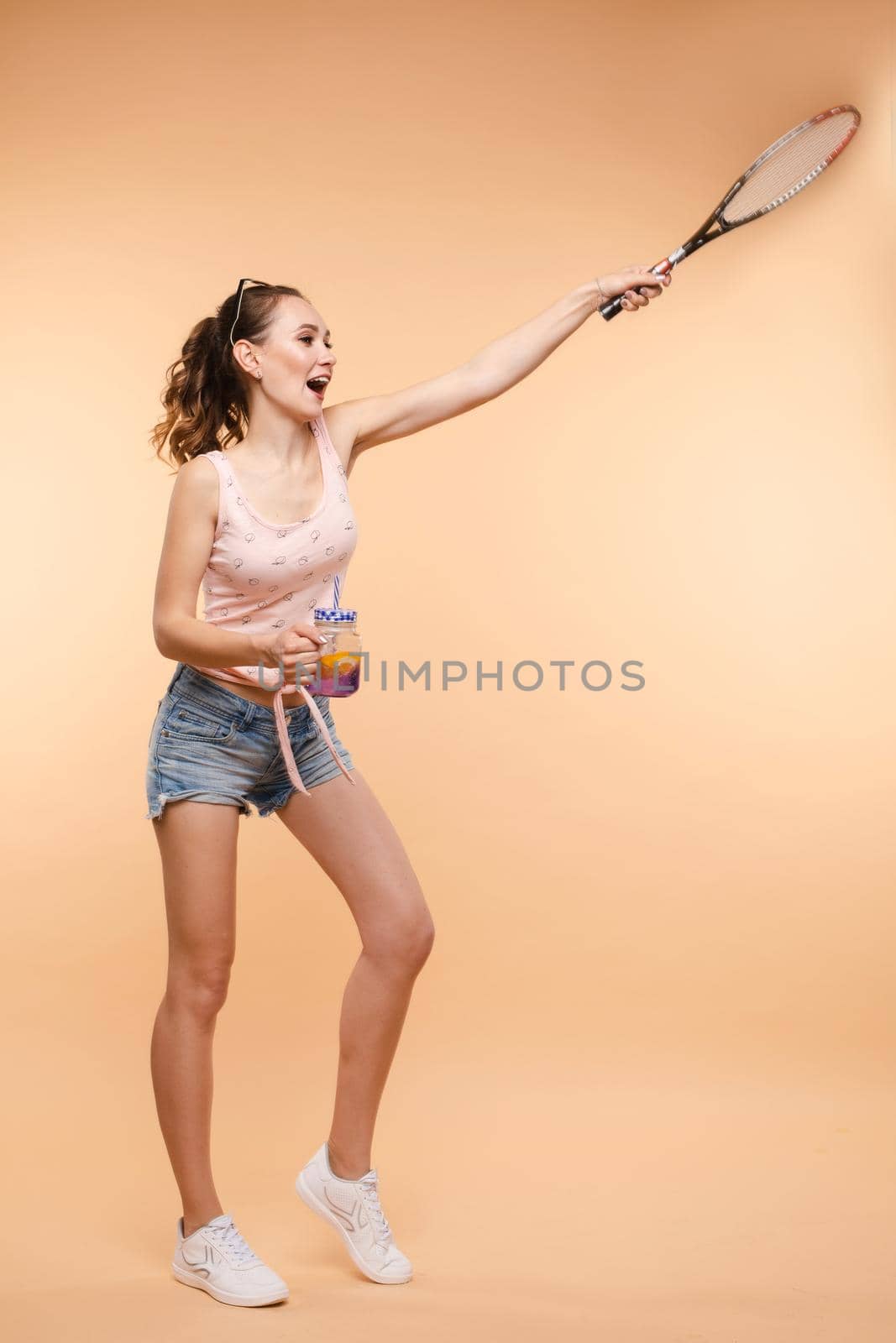 A beautiful woman in a bright outfit, denim shorts with a racket in her hands in the studio. Summer.