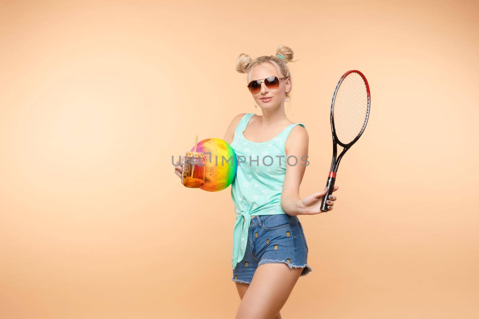 A beautiful woman in a bright outfit, denim shorts with a racket in her hands in the studio. Summer.