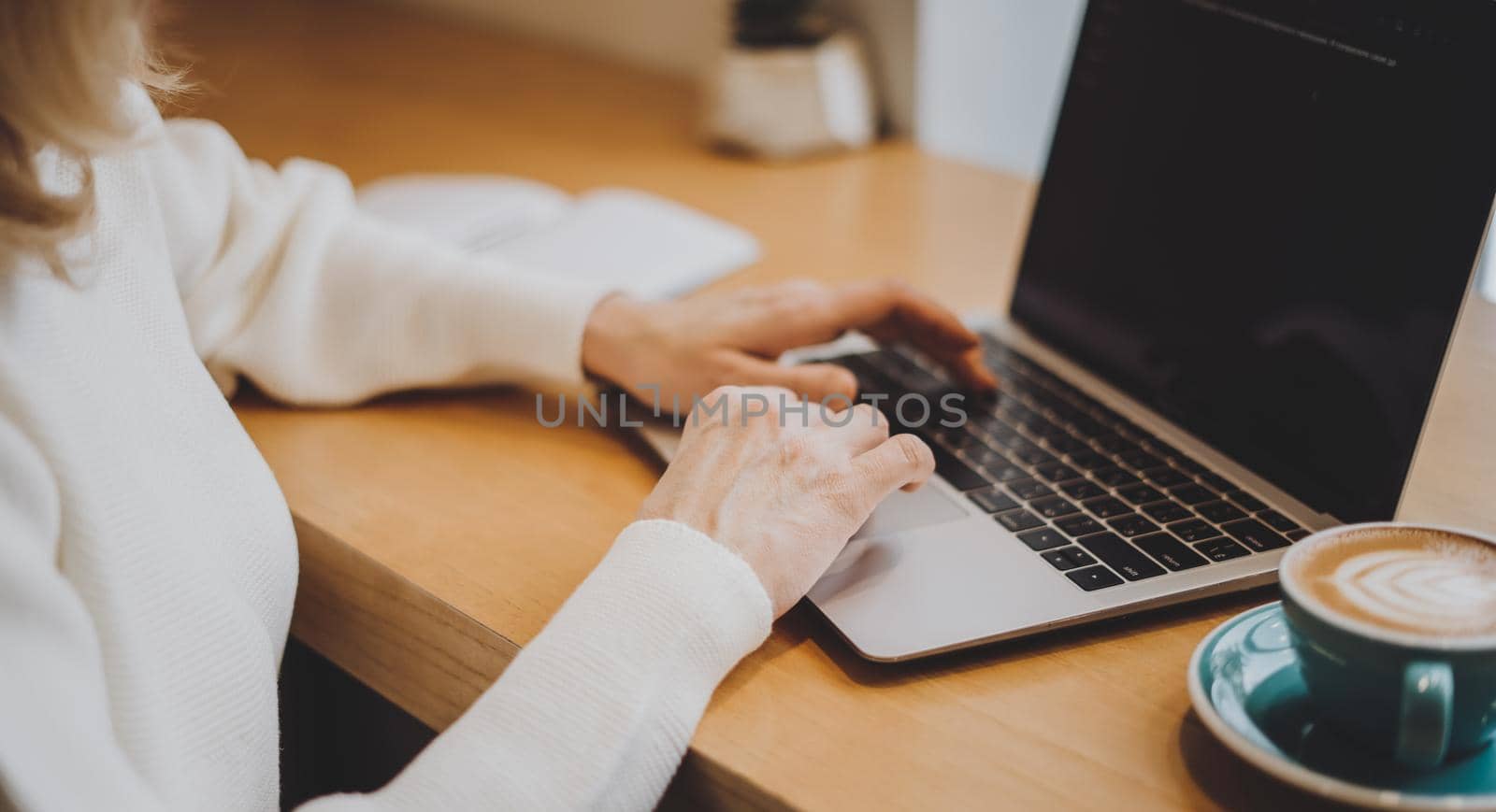 Mature adult woman hands, sitting in cafe with coffee mug and working online on laptop. Businesswoman typing on notebook computer in coworking space in roasters coffee shop, close up