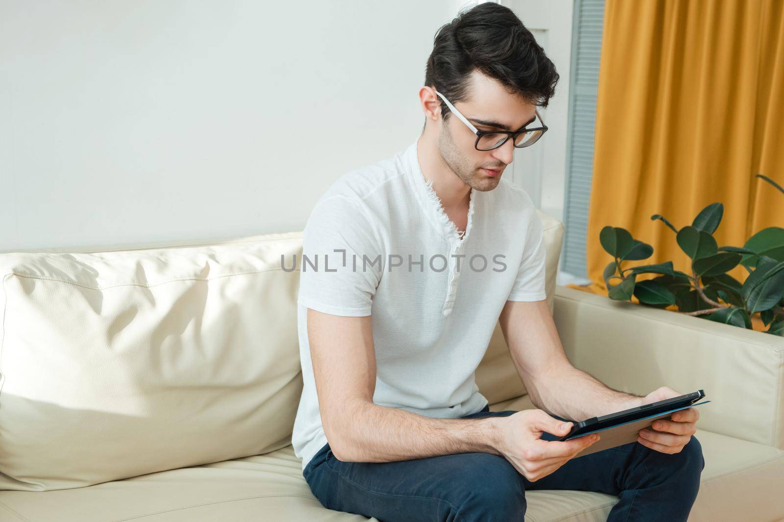 Young man browsing internet or checking social media on tablet, relaxing on sofa at home. by etonastenka