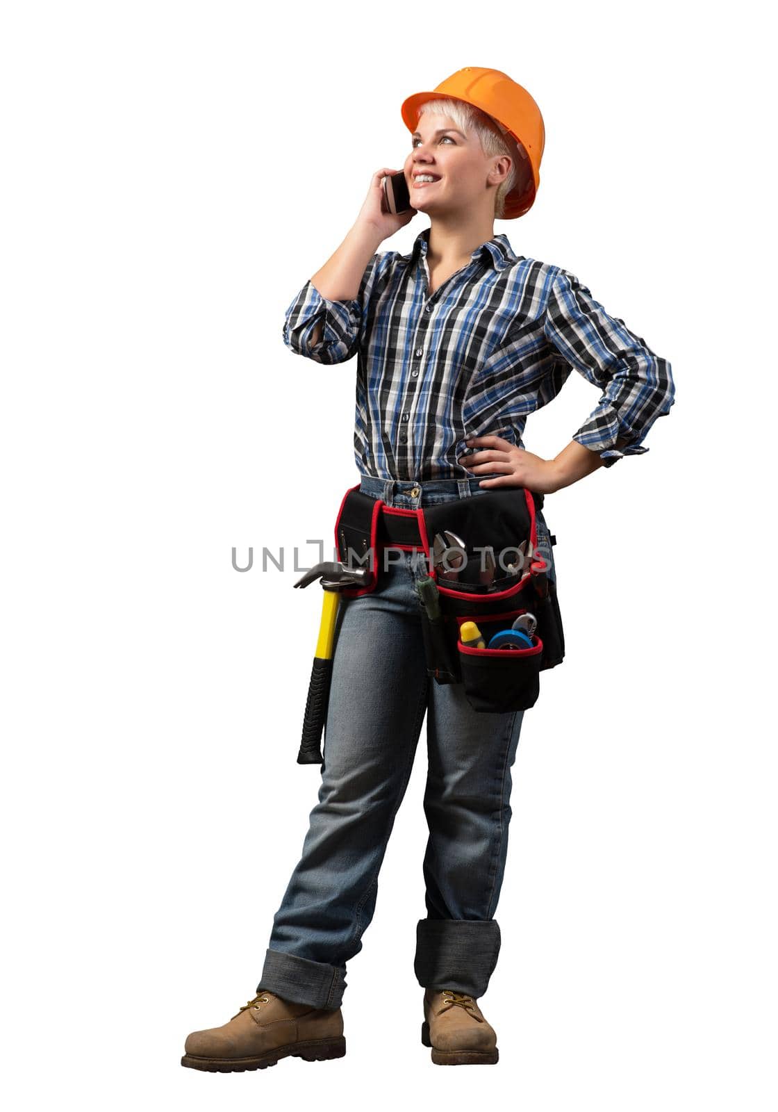Attractive blonde woman in workwear and hardhat talking on smartphone. Young engineer in checkered blue shirt and jeans isolated on white background. Business communication and conversation.