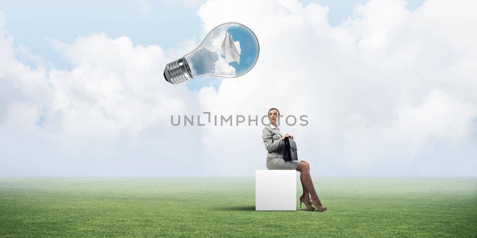 Elegant businesswoman with suitcase in hand sitting on white cube and big glass bulb