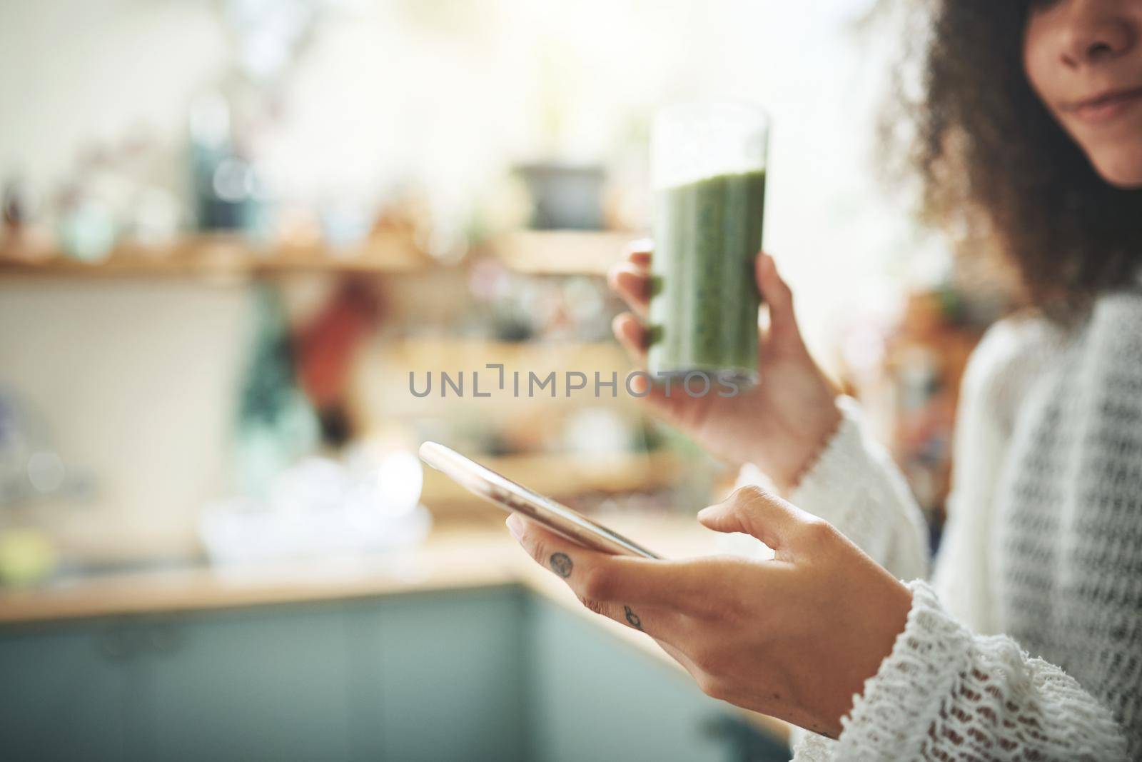 Beautiful young girl browsing online while enjoying her healthy green smoothie