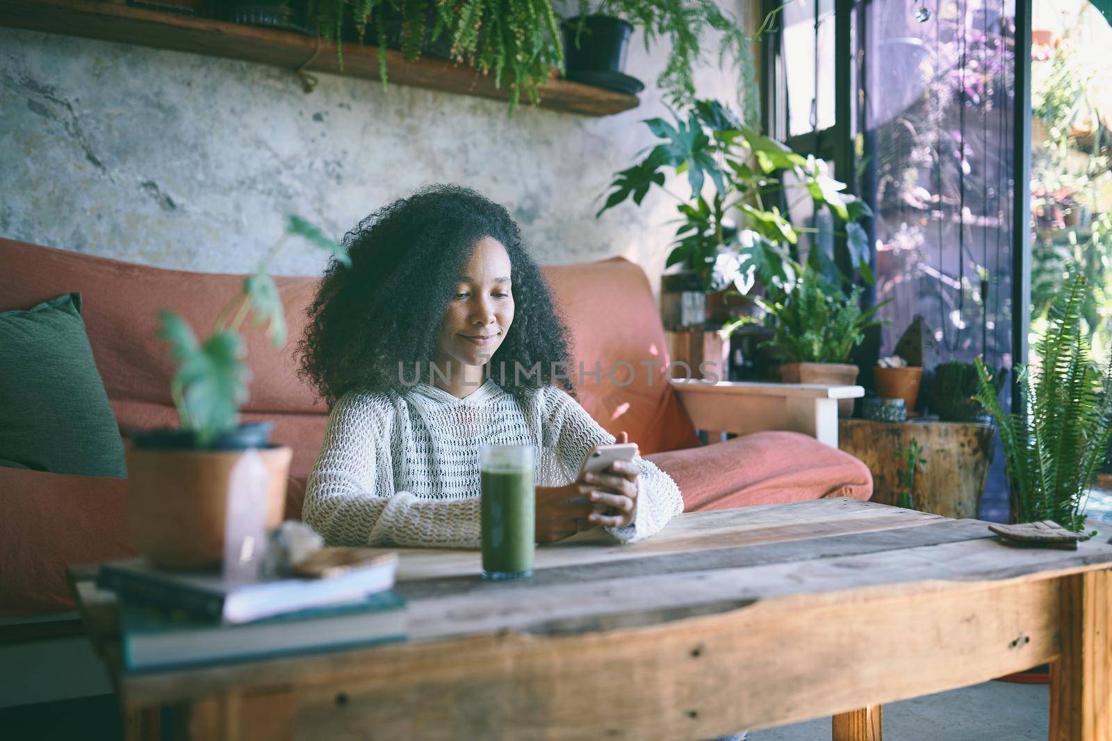 Beautiful girl browsing on social media while enjoying her green smoothie in her lounge