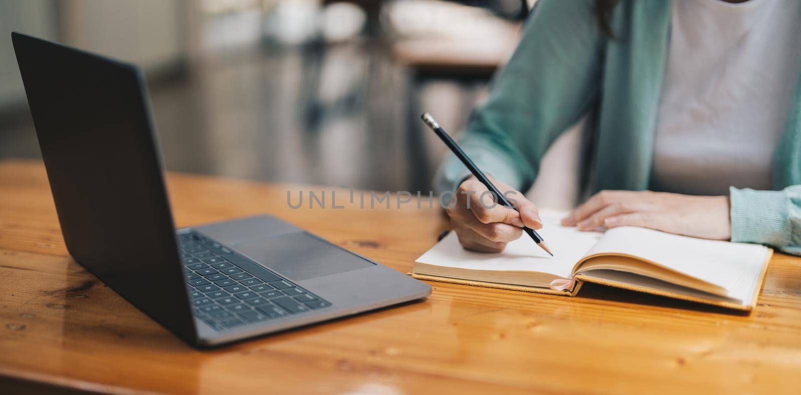 Cropped photo of woman writing making list taking notes in notepad working or learning on laptop indoors- educational course or training, seminar, education online concept by nateemee