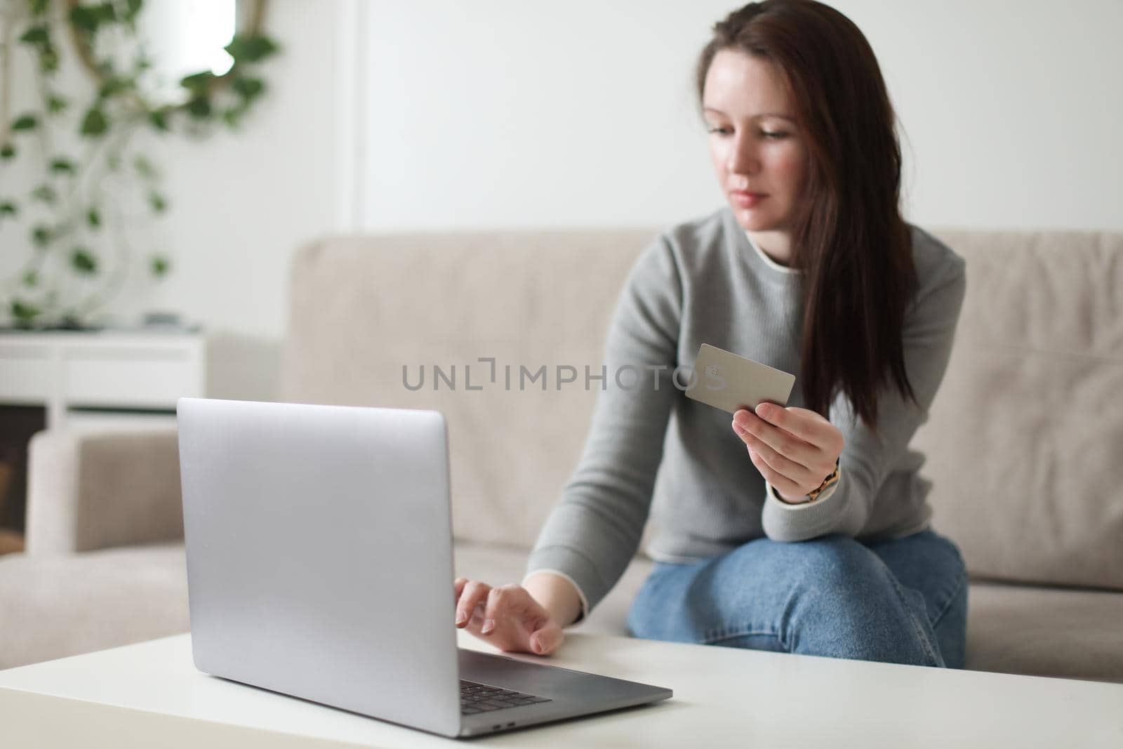 Young woman holding credit card and using laptop at home. Paying online, home shopping, internet banking, electronic store concept.