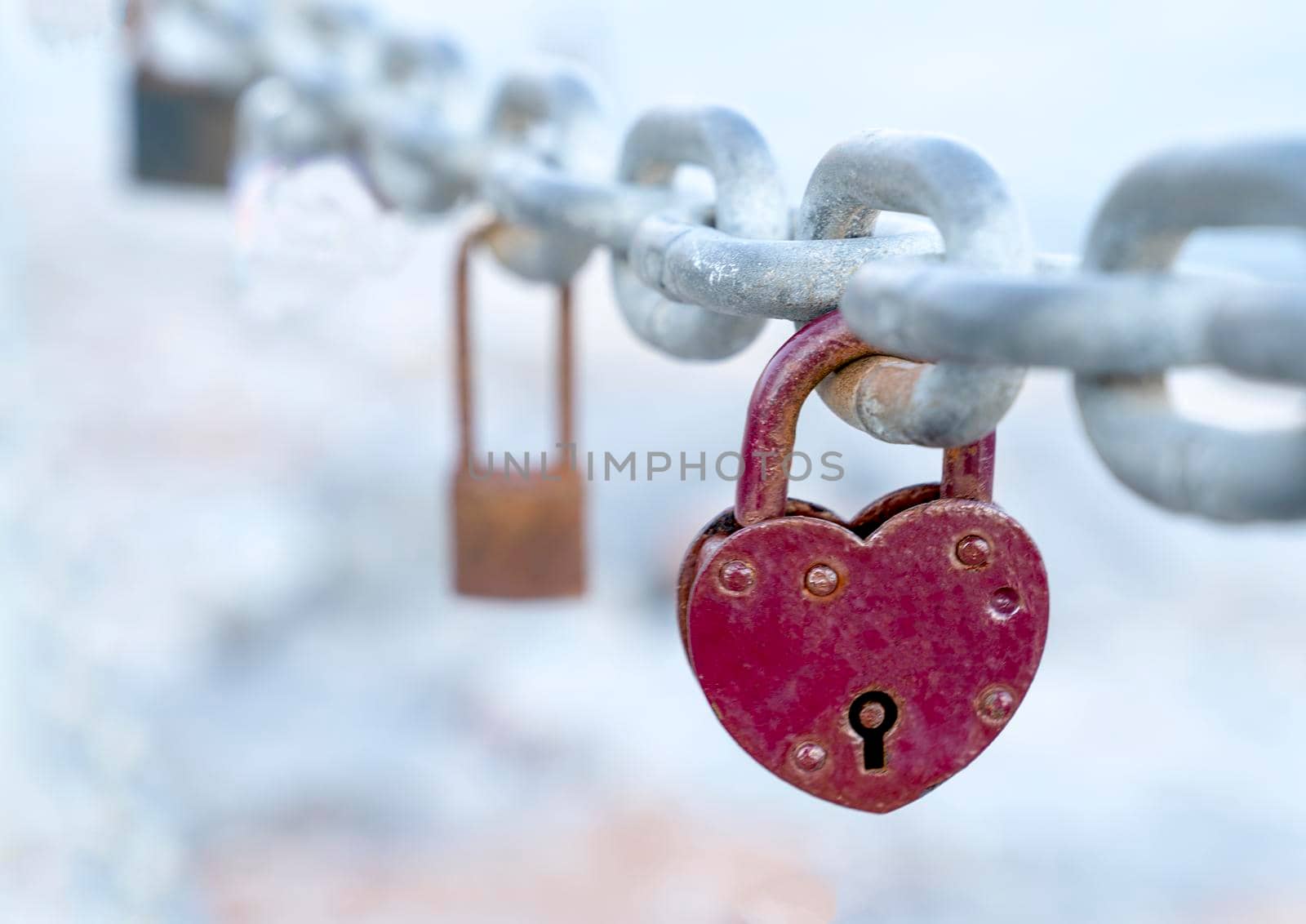 A red heart-shaped lock hangs from the bridge chain. The wedding custom is a symbol of eternal love. Close-up.