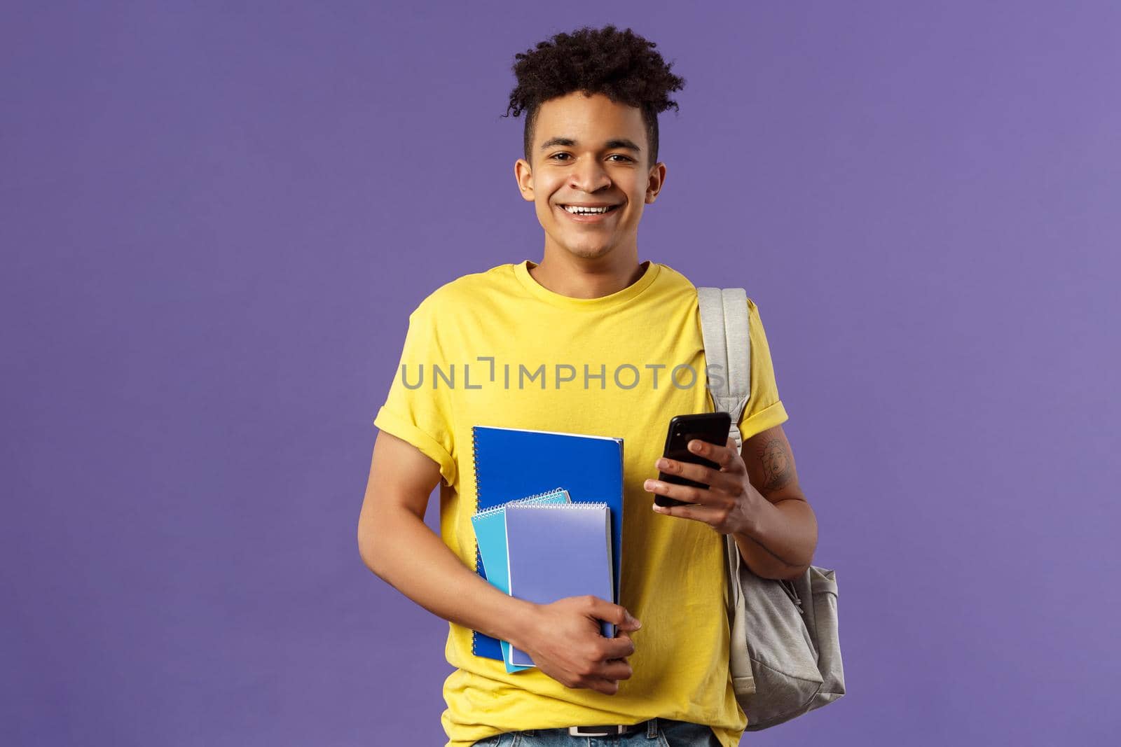 Back to school, university concept. Portrait of cheerful young handsome male student wearing backpack on shoulder, hold notebooks and studying books, texting friend mobile phone.