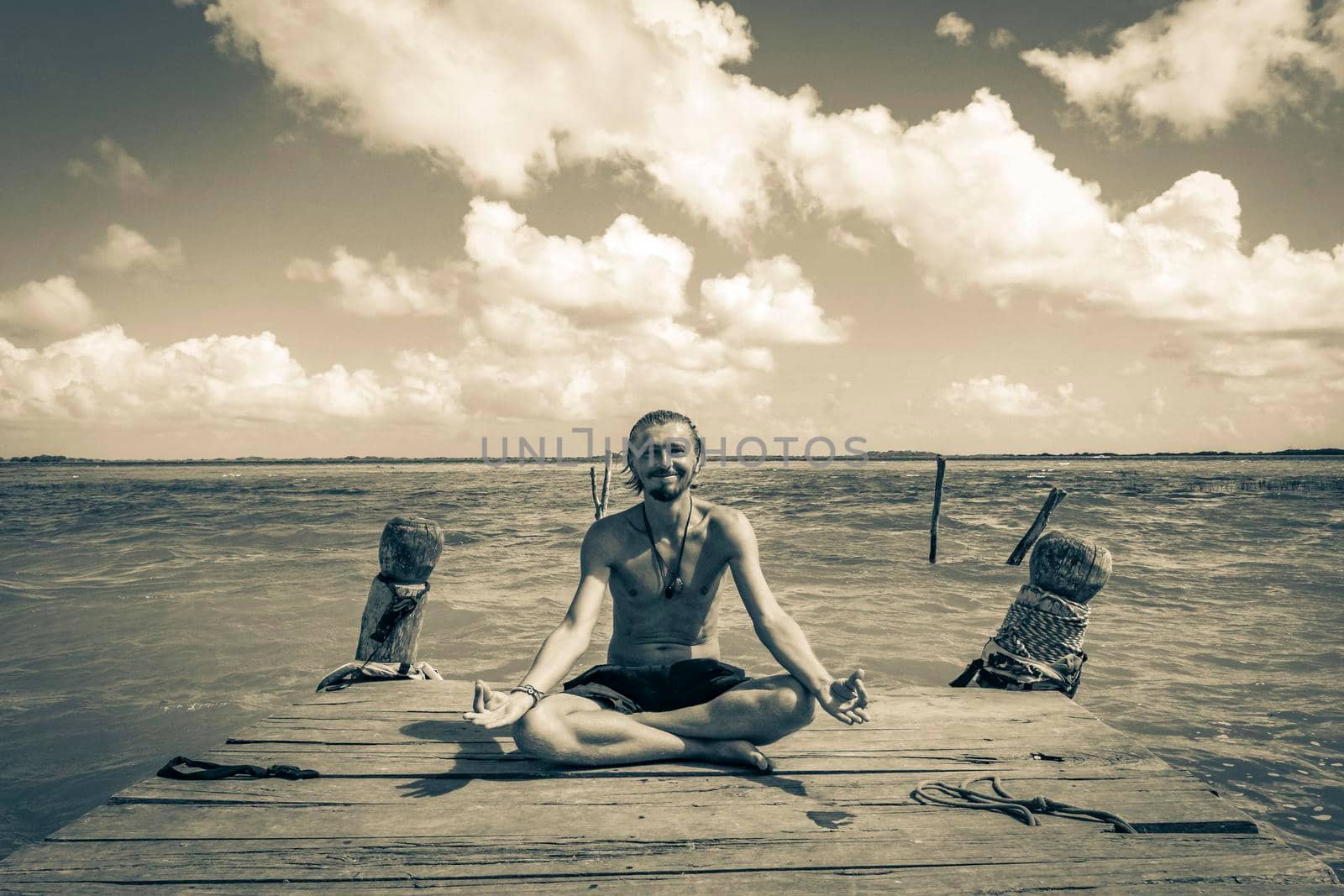 Black and white picture of a traveler and tourist meditate on boat jetty pier at the panorama view to the Muyil Lagoon with turquoise water in the tropical jungle Sian Kaan National park Muyil Mexico.