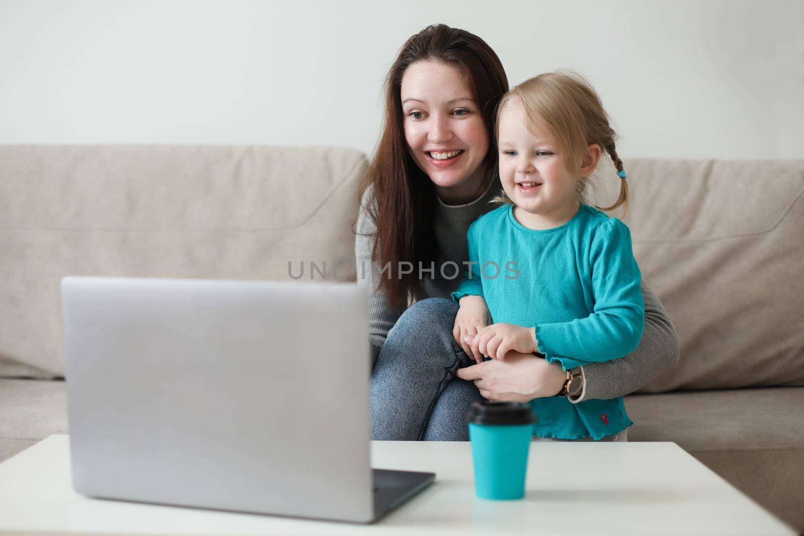Mother and her daughter using video chat on laptop sitting on cozy sofa at home, watching video, having fun
