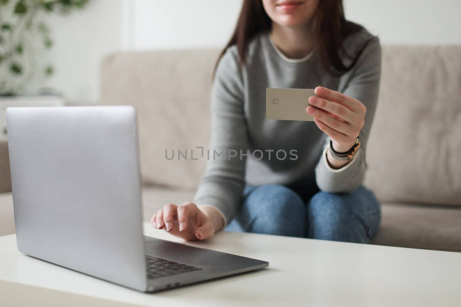 Young woman holding credit card and using laptop at home. Paying online, home shopping, internet banking, electronic store concept.
