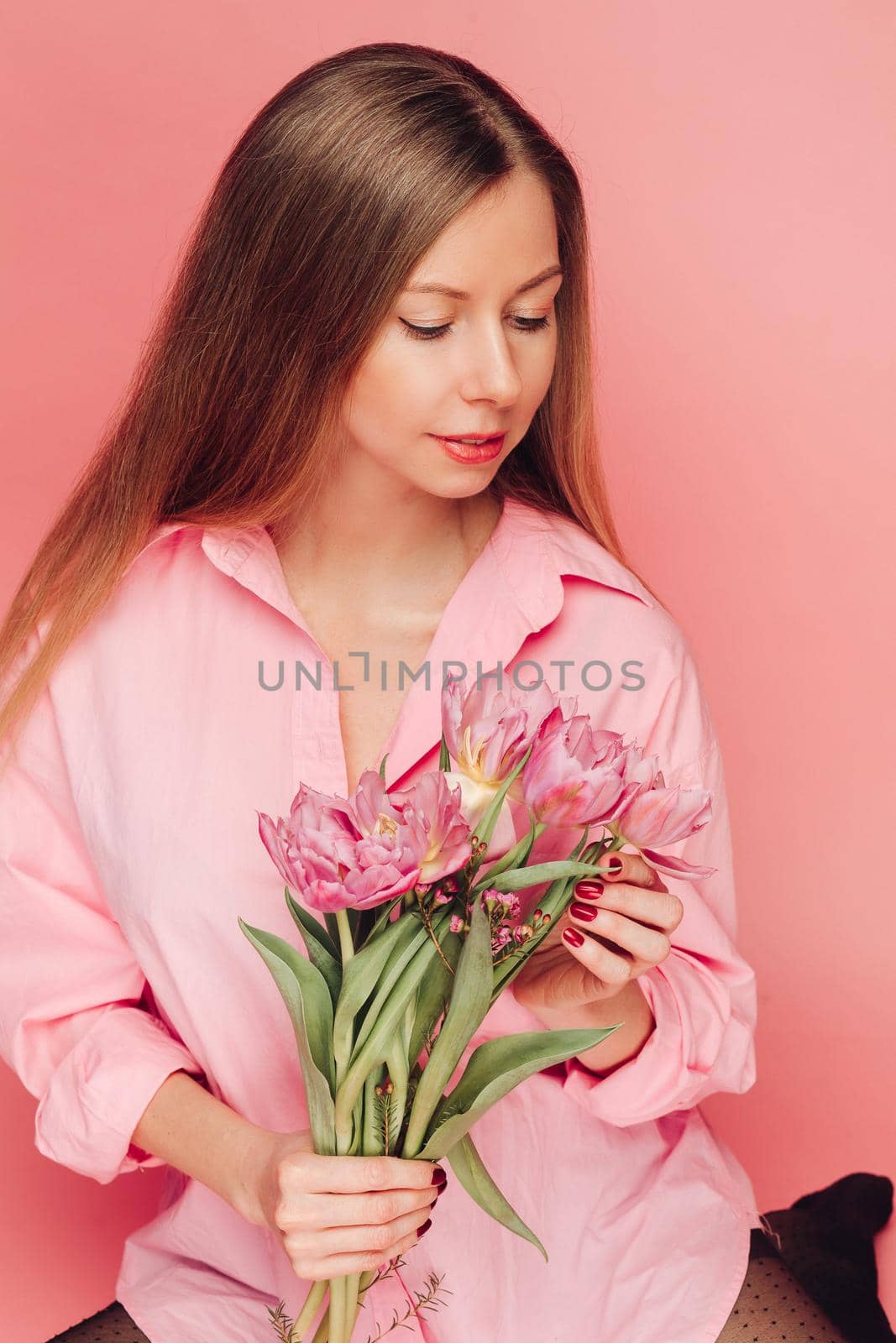 A sweet charming woman with flowers in a pink dress on a pink background smiles, happiness and luck by StudioLucky