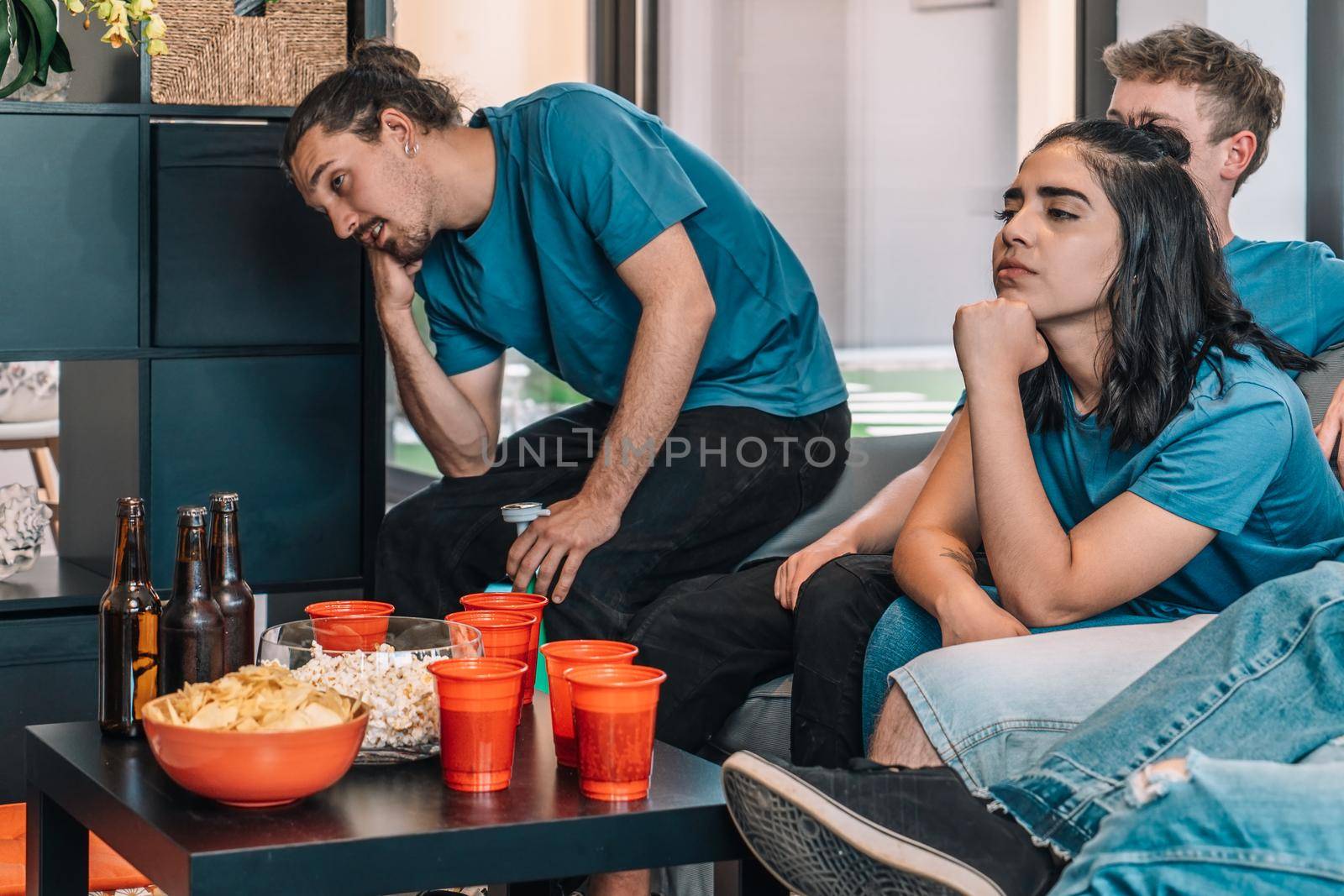 Football fans saddened by their team's defeat. Friends watching football in living room concept of leisure. concept of friendship. group of six people, friendly relationship, divided teams, red and blue, competitive.