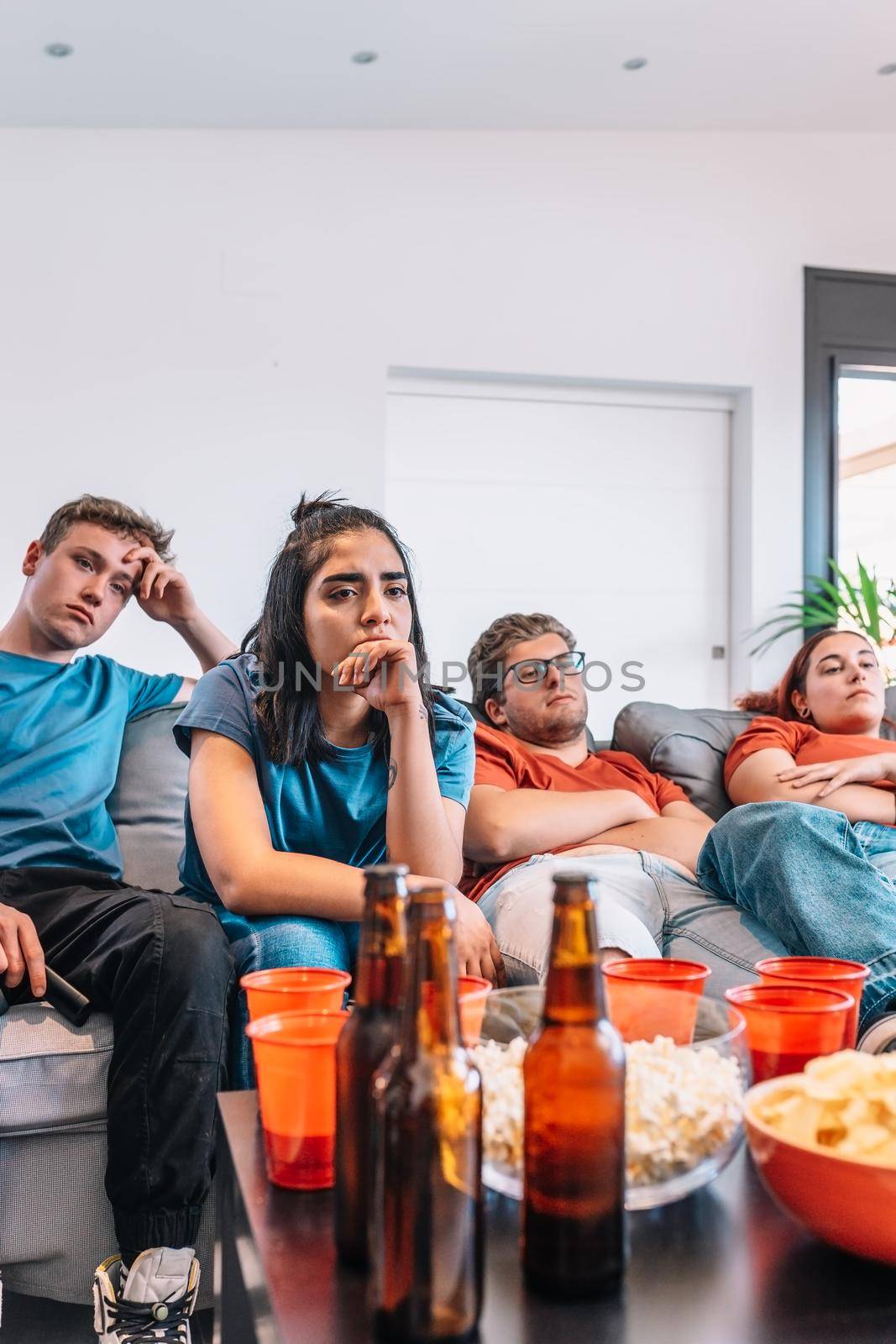 sad friends watching TV because their football team lost the game. upset young people at a house party. by CatPhotography