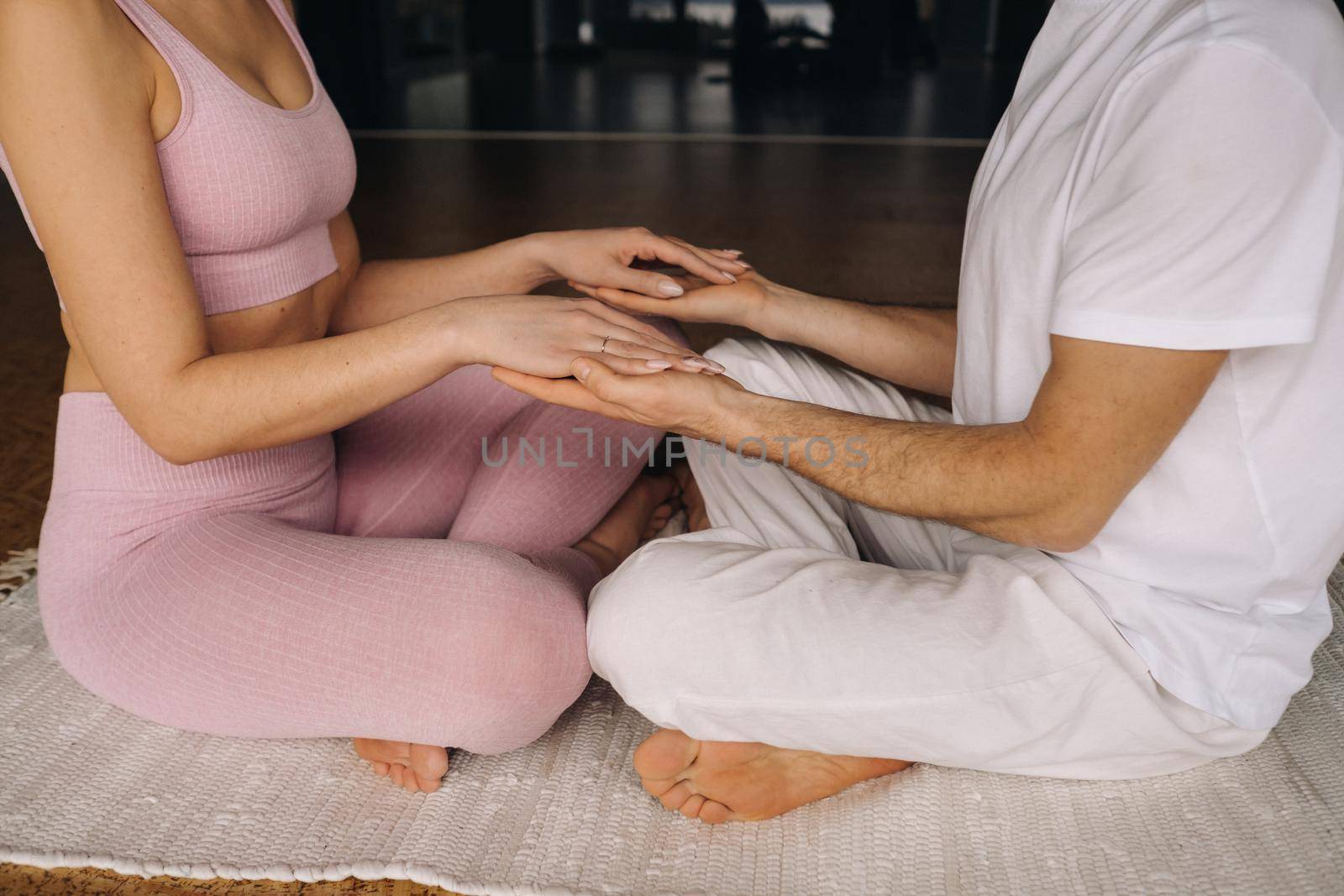 a woman and a man are engaged in pair meditation holding hands in the gym by Lobachad