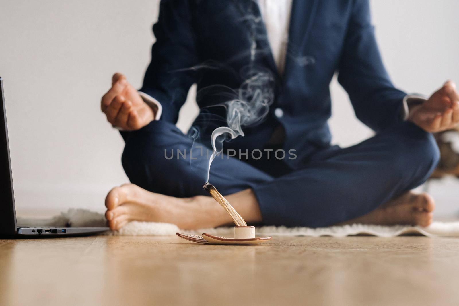 A man in a formal suit meditates while sitting in a fitness room with a laptop.