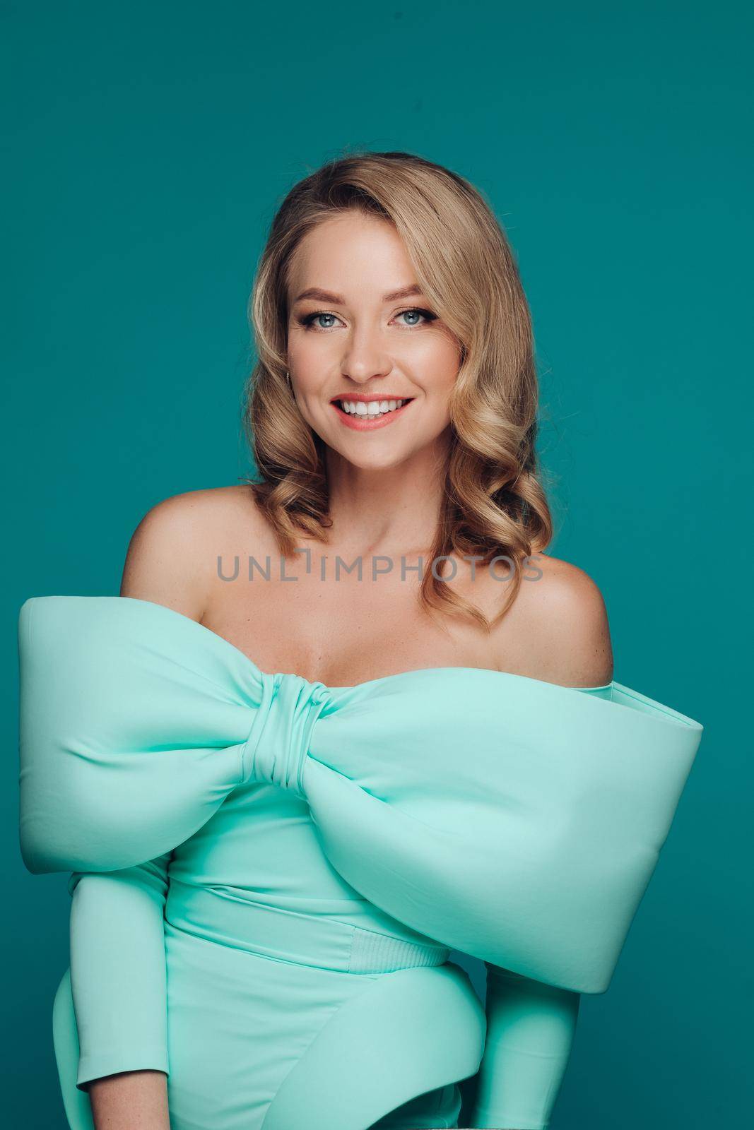 Beautiful elegant woman in a bright tiffany dress with a bow on her chest in the studio on a turquoise background