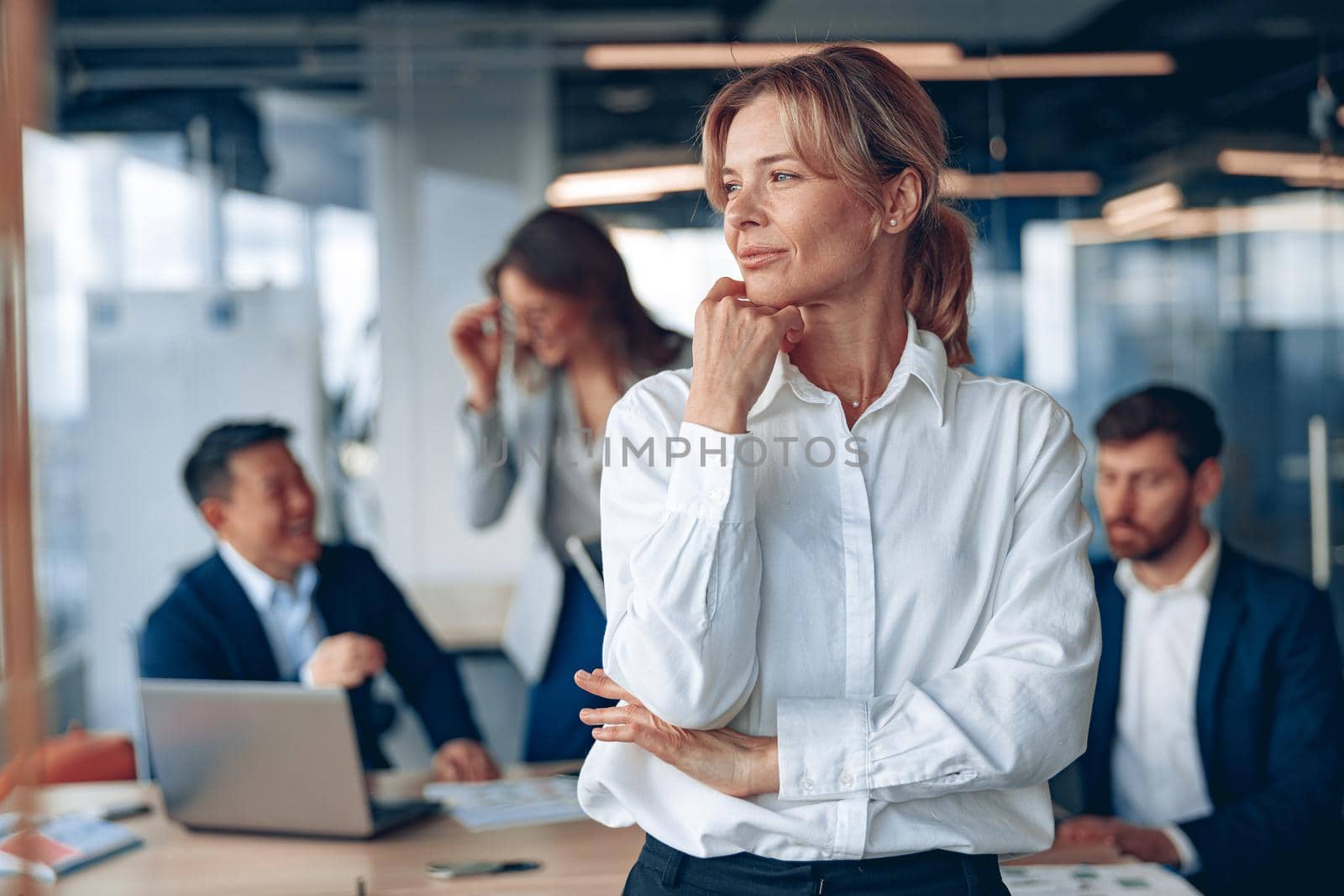 portrait of confident female boss looking at side with her colleagues at background in office.