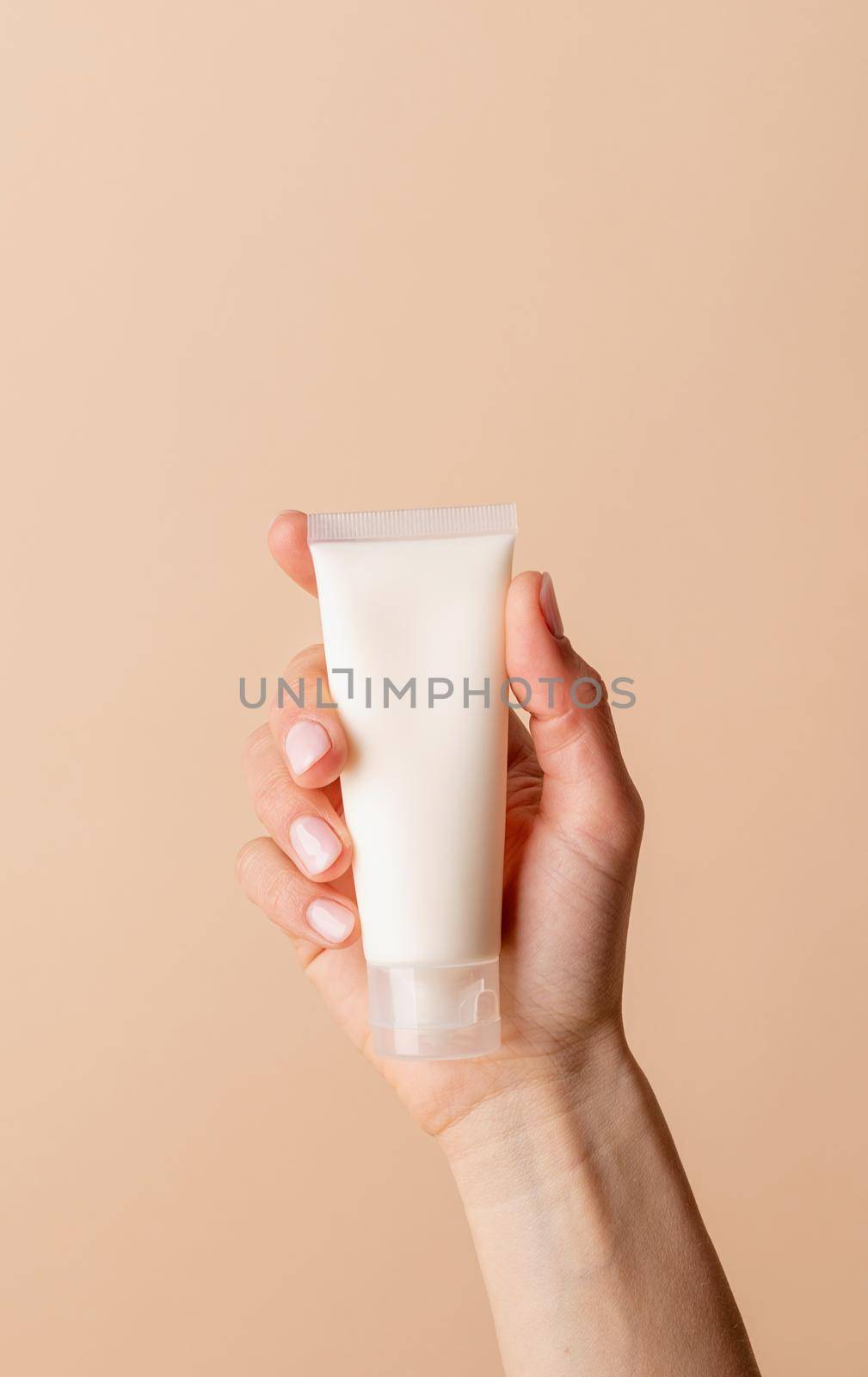 Natural cosmetics. Face cream Mock-Up. Female hand holding white cream tube on beige background