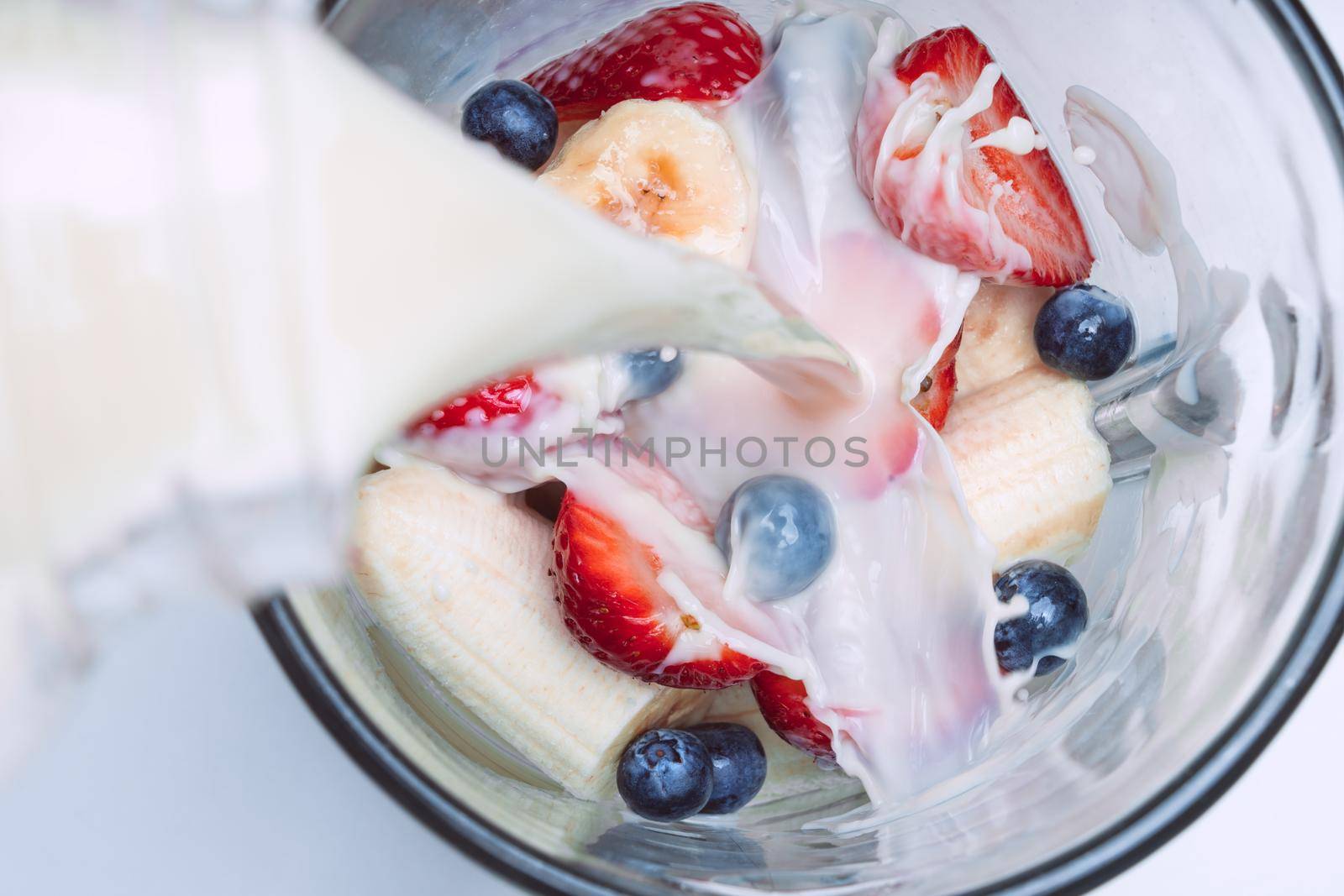 Making smoothie or milkshake in blender. Pouring milk in a blender with fruits. Vegan smoothie with almond milk by DariaKulkova