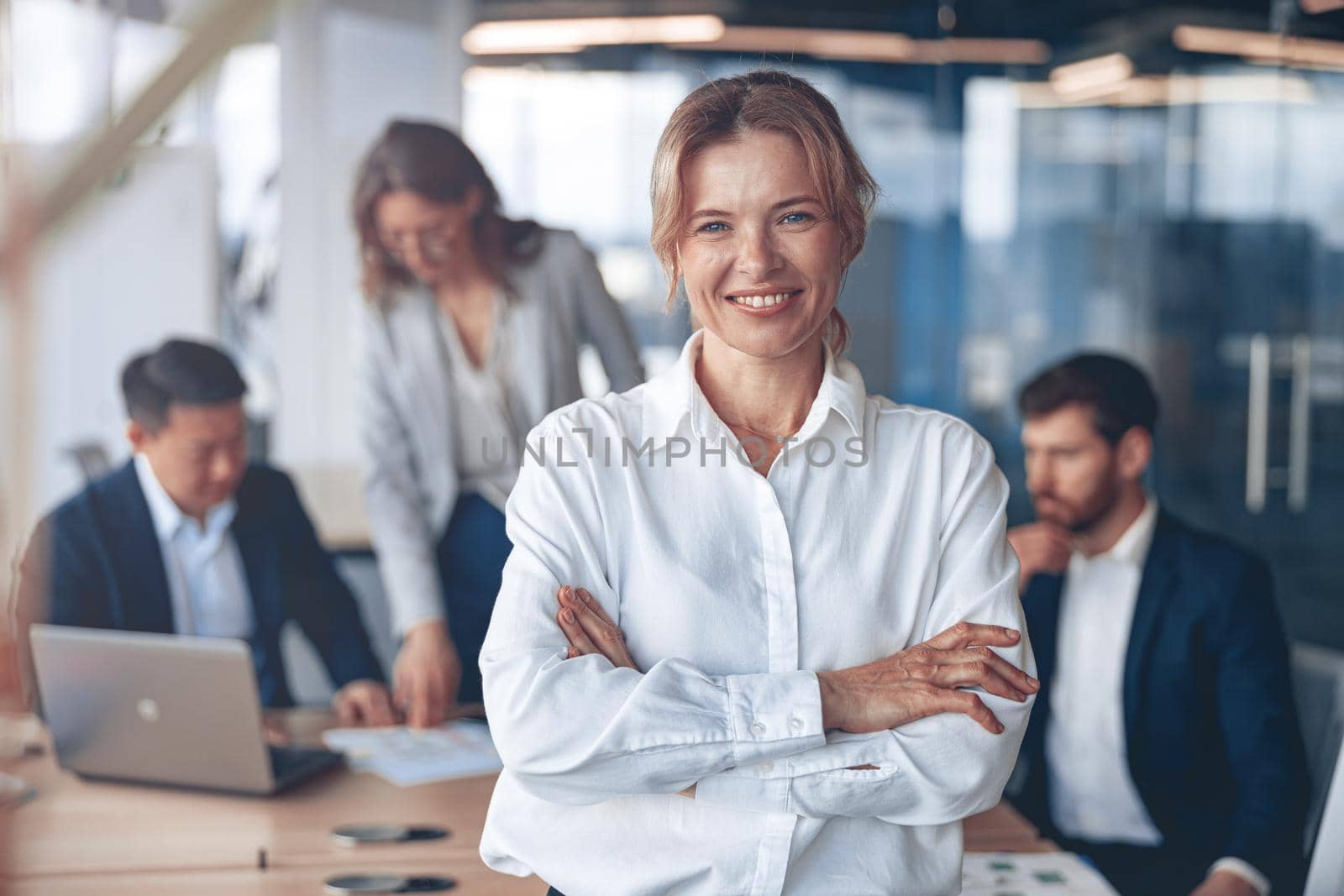Portrait of beautiful smiling mature businesswoman with her colleagues on background in office by Yaroslav_astakhov