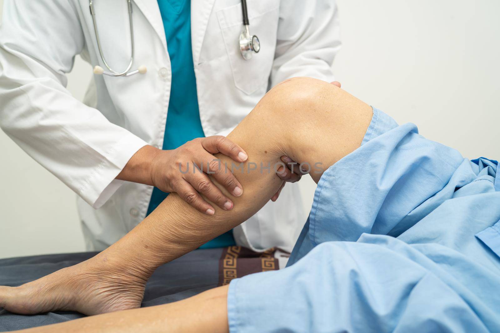 Asian doctor physiotherapist examining, massaging and treatment knee and leg of senior patient in orthopedist medical clinic nurse hospital. by pamai