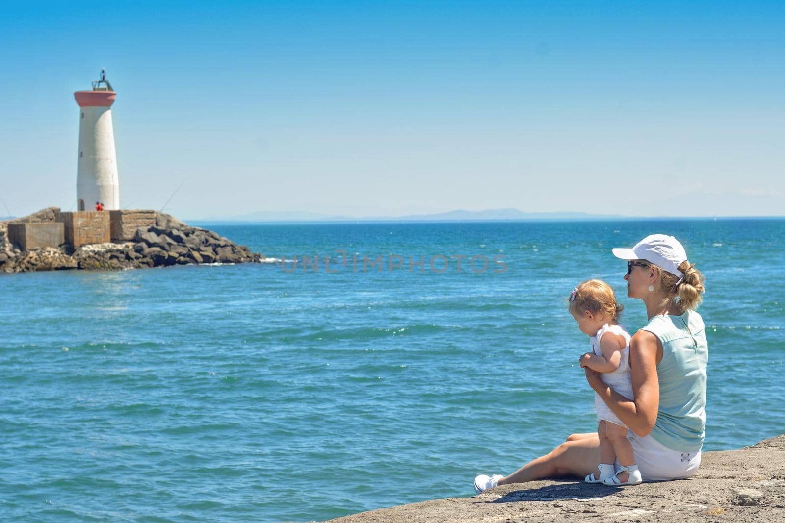 Mother and daughter on the pier on the Mediterranean coast with lighthouse