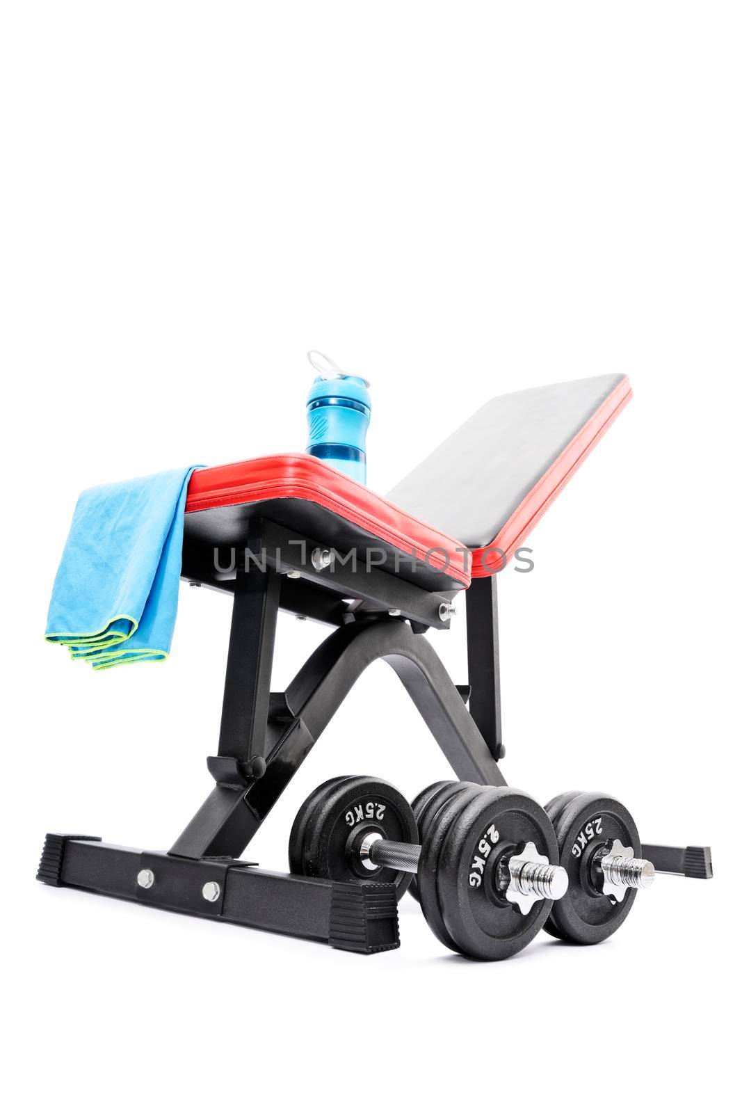 Dumbbells beneath a workout bench with towel and water bottle by Mendelex